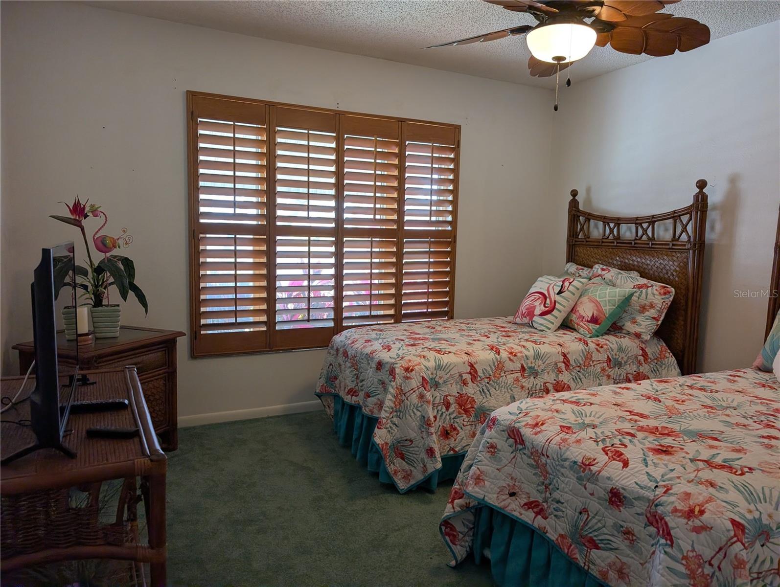 Guest bedroom features carpeting, ceiling fan and plantation shutters.