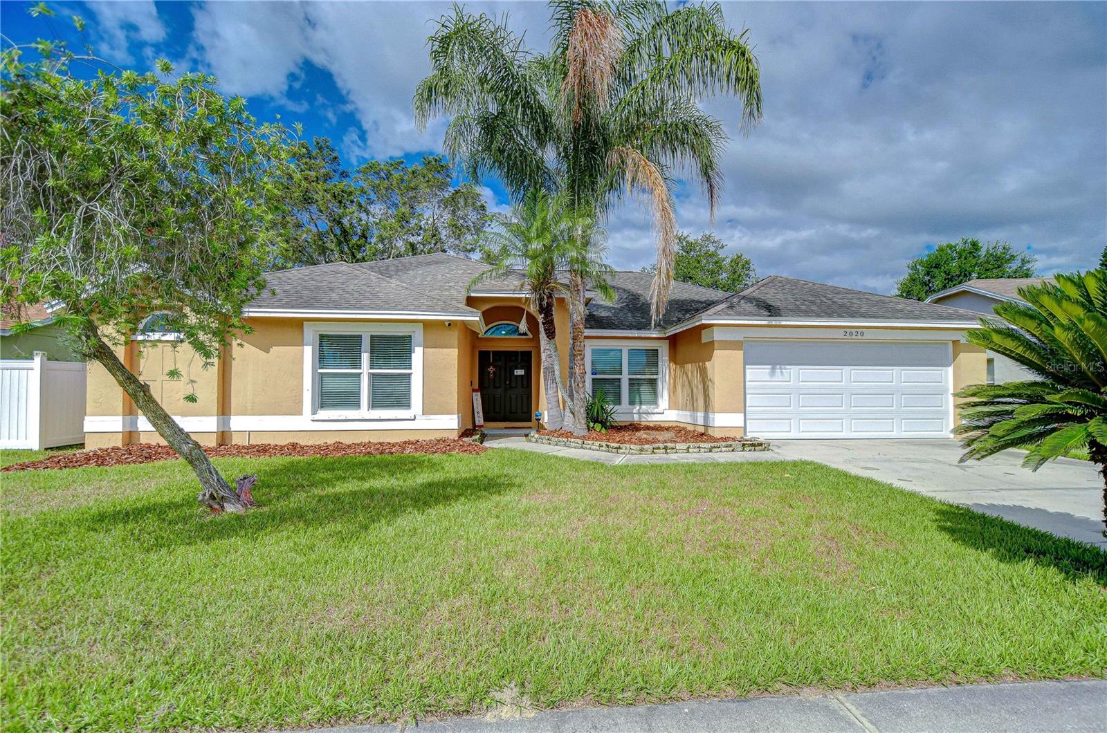 Inviting single-story home with arched entry, two-car garage, and lush palm-lined front yard.