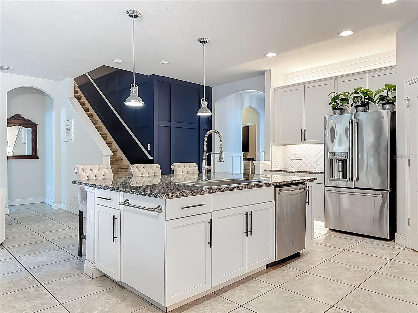 Kitchen boasts white wood cabinetry, granite countertops, a striking herringbone subway tile backsplash, stainless steel appliances, an oversized island with additional cabinetry and a breakfast bar, under-cabinet and over-cabinet LED lighting, a spacious eat-in dining area, and a custom walk-in pantry