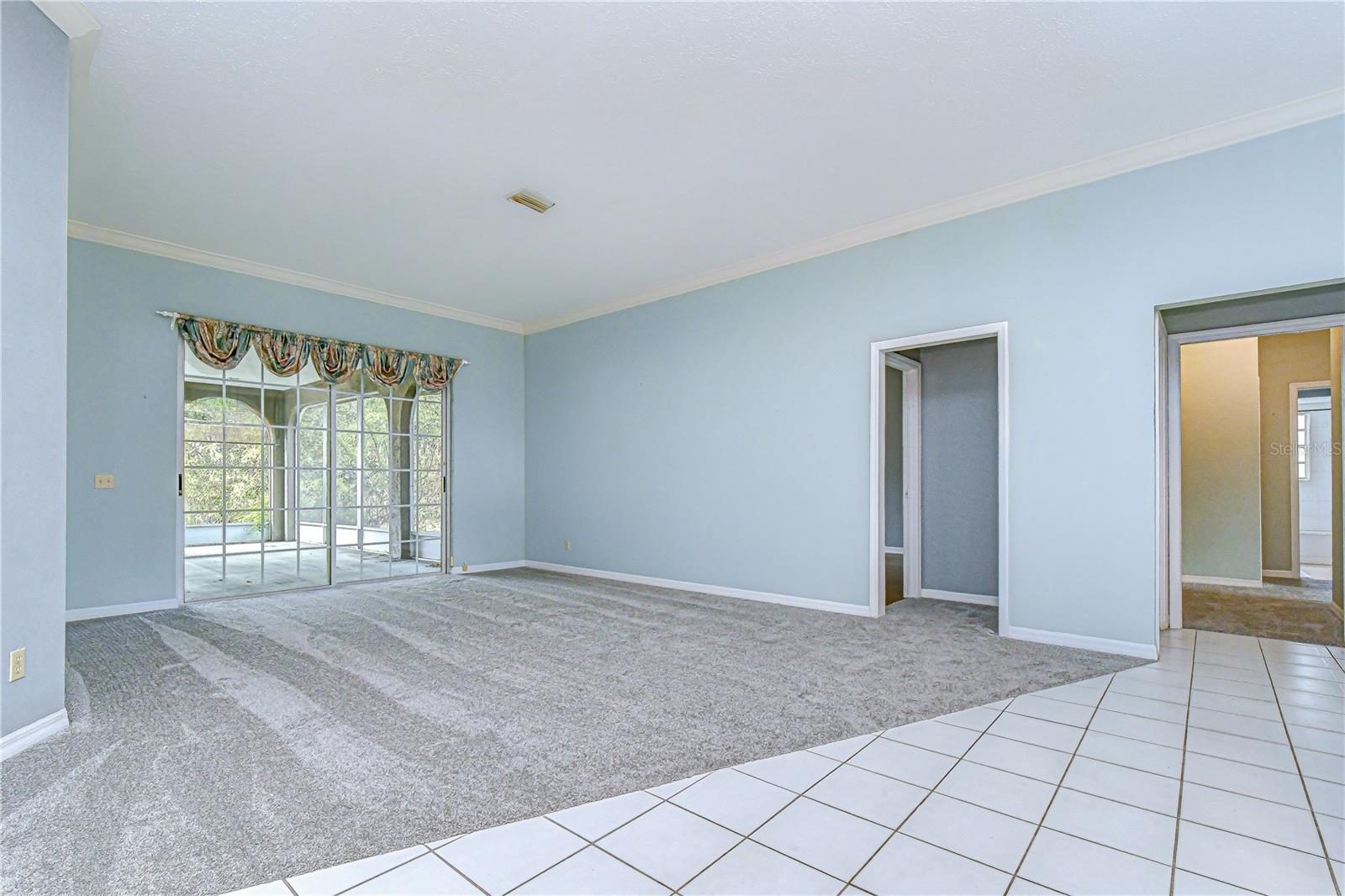 Airy living room with crown molding, and sliding glass doors to a bright lanai.