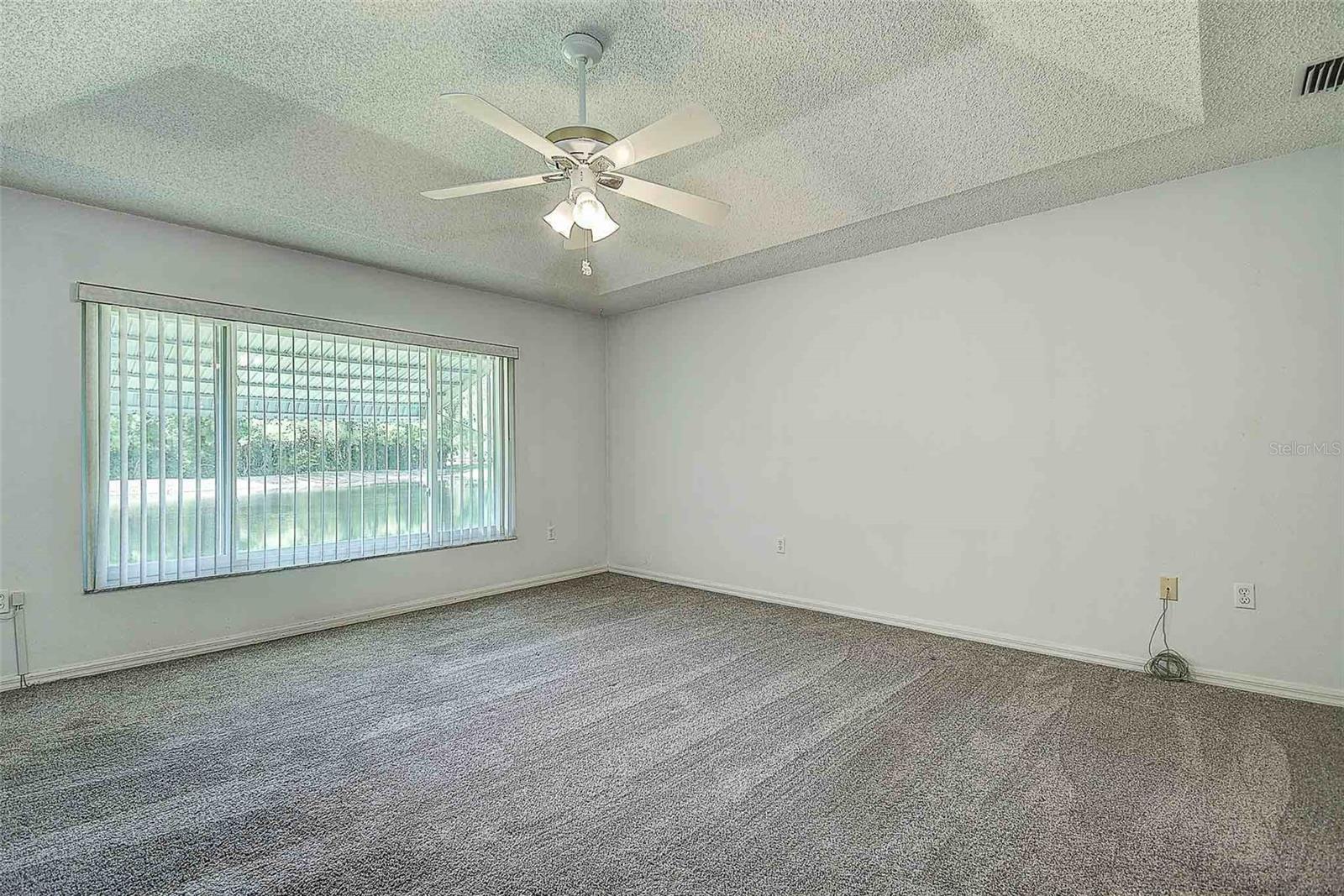 Primary bedroom with tray ceiling, ceiling fan and large picture window overlooking the pond view!