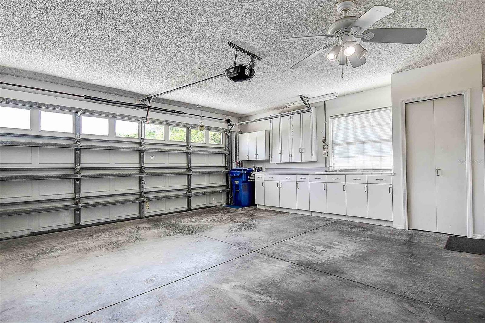 Additional cabinets and workspace inside garage, with ceiling fan.