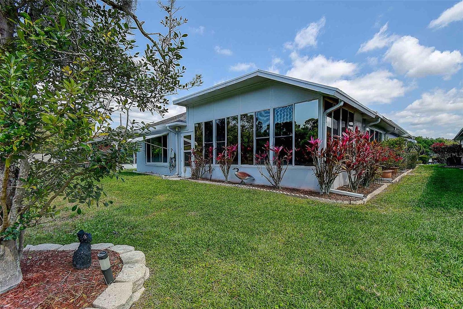 Exterior view of enclosed/covered Florida room with landscape.