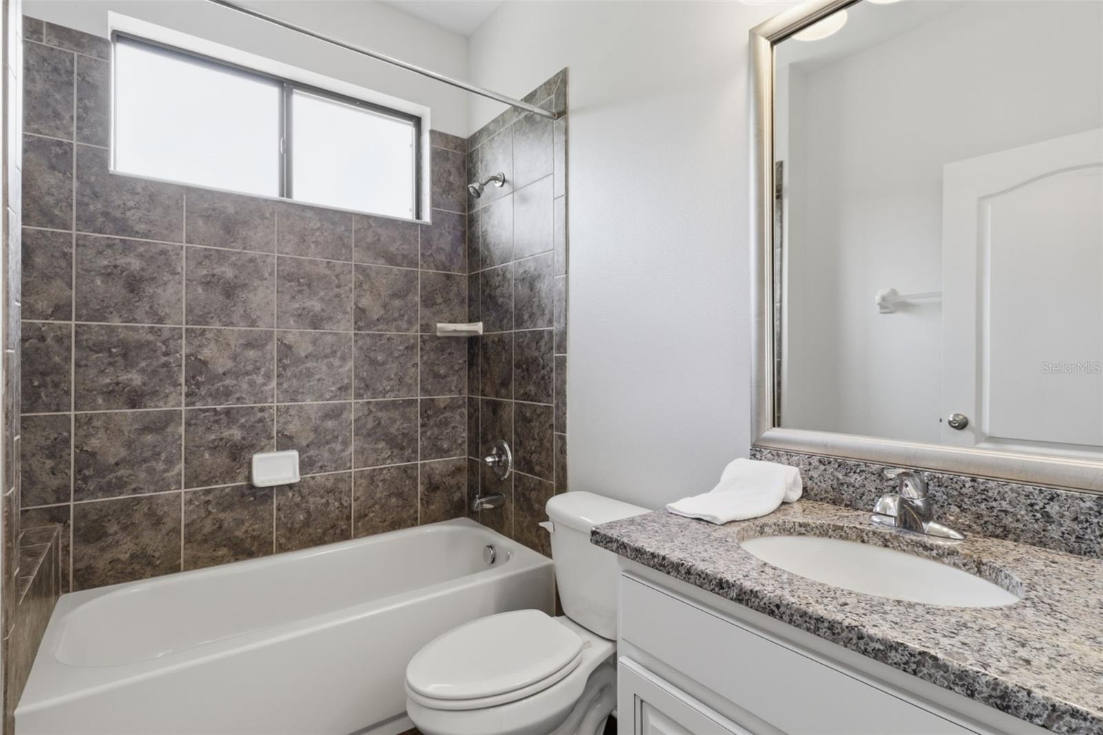 Full bathroom featuring granite countertops, a tub/shower combination, and clean, modern finishes.