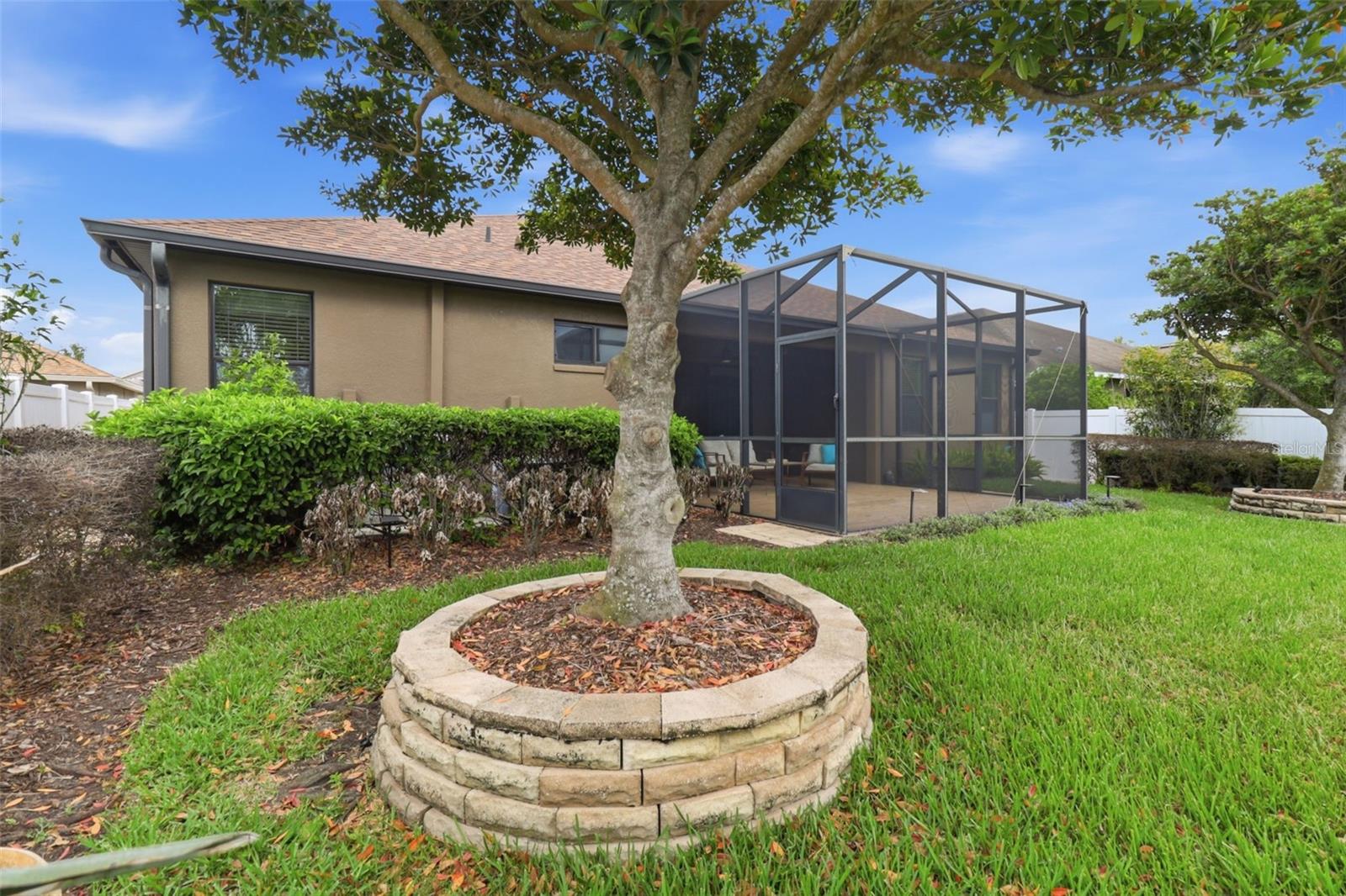 Spacious backyard with mature landscaping and a fully fenced yard, overlooking peaceful waterfront views and the screened lanai—perfect for outdoor living and entertaining.