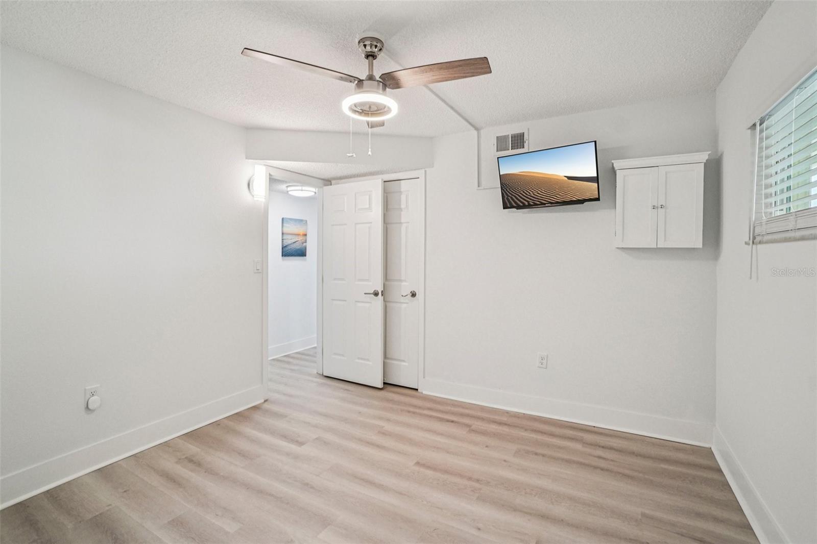 Bedroom #2 – A second angle of this well-proportioned bedroom showcases the double closet doors, wall-mounted TV, built-in cabinet for additional storage, and easy access to the hallway — offering both comfort and practicality in a fresh, move-in-ready finish.
