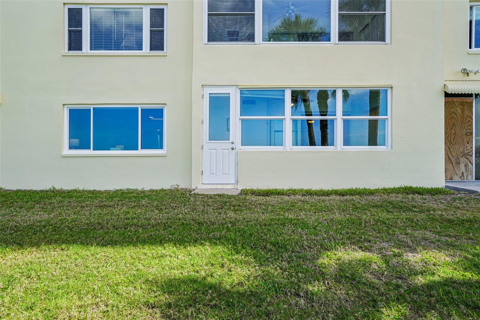 Unit Exterior / Waterside Entry – Unit 107's ground-floor waterside exterior features large picture windows that flood the interior with natural light and reflect the stunning water views just beyond — with a private side entry door offering convenient direct outdoor access.