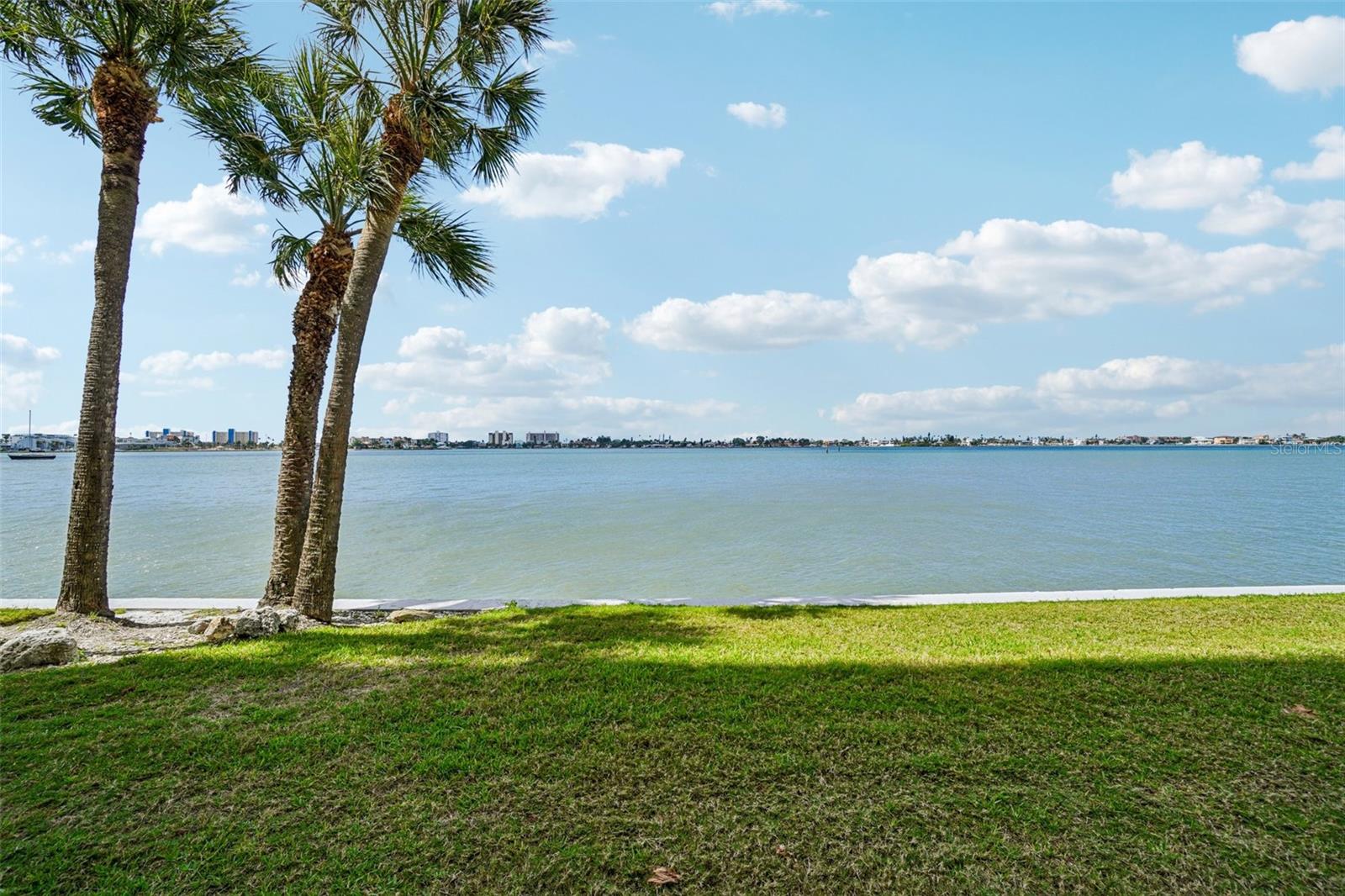 Waterfront Lawn & Open Water View – A lush, palm-shaded lawn stretches to the water's edge, offering a serene outdoor escape just steps from your door — an idyllic setting for relaxing, watching sailboats drift by, or simply soaking in the Florida sunshine.