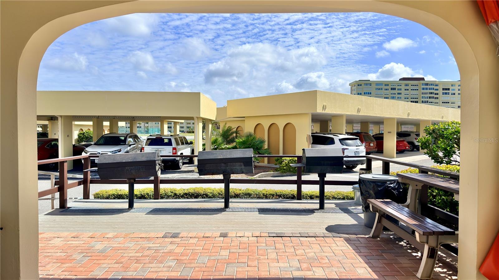 Community BBQ & Grilling Area – The community's covered outdoor grilling area features multiple charcoal BBQ grills, picnic seating, and a brick paver patio framed by a classic arched entryway — a great spot for casual cookouts and enjoying the Florida outdoors with neighbors.