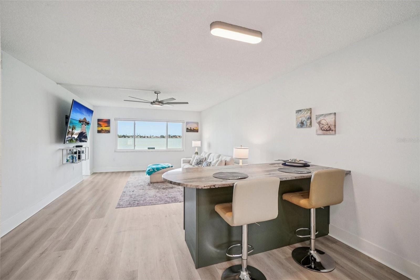 Dining Island & Living Room ViewThe curved stone-top dining island with bar seating anchors the heart of the home, offering a front-row seat to the water view beyond — an ideal spot for morning coffee or casual meals with a coastal backdrop.