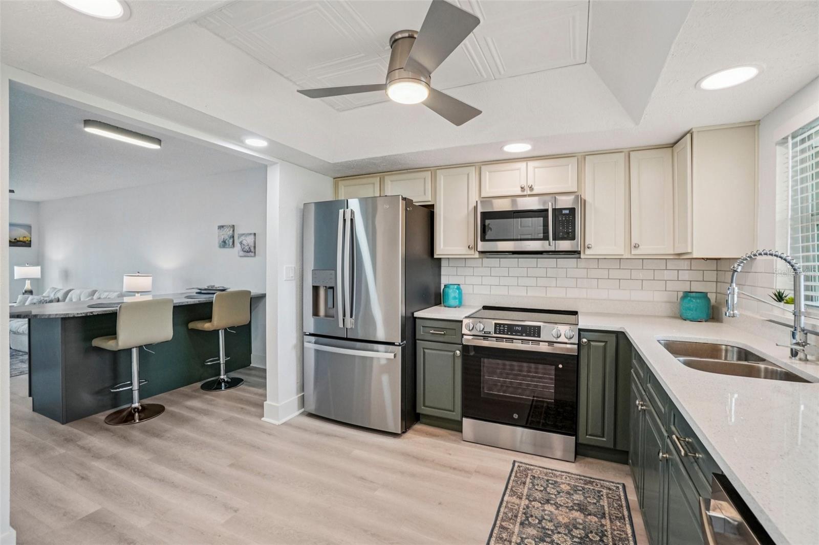 Kitchen – This beautifully updated kitchen features two-tone cabinetry with sage green lower cabinets and crisp cream uppers, quartz countertops, a classic subway tile backsplash, and a full suite of stainless steel appliances — all topped with a coffered ceiling detail and modern ceiling fan for an elevated coastal feel.