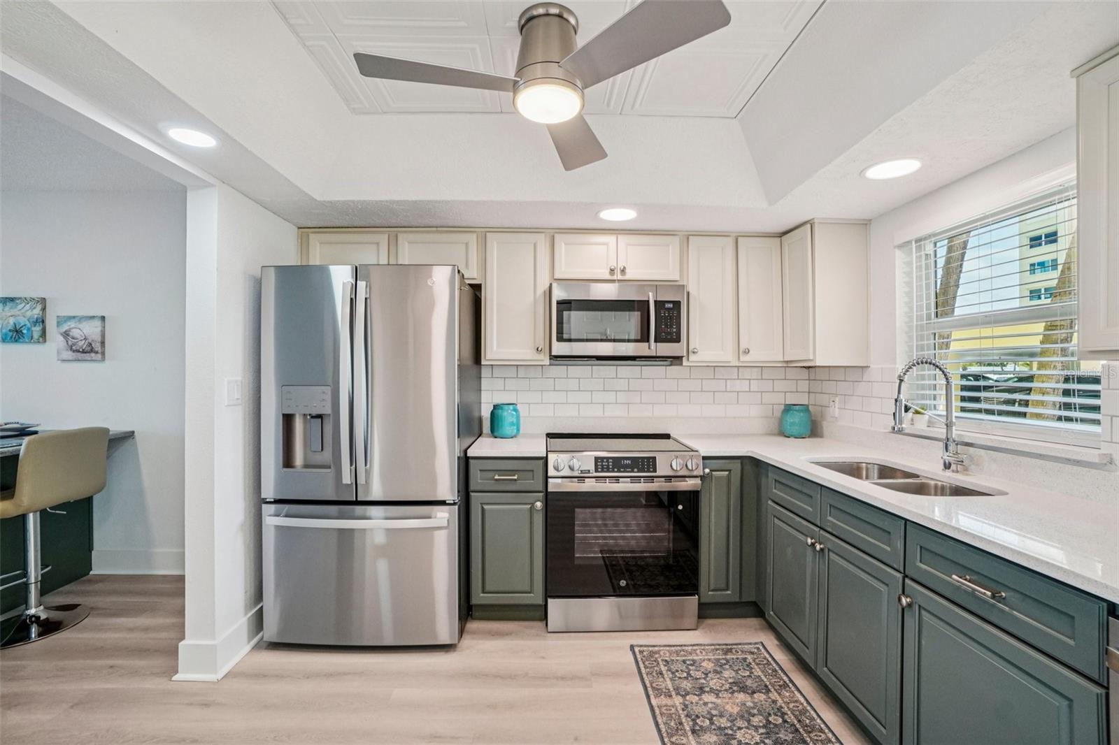 Kitchen (Detail View) – A closer look at the kitchen reveals thoughtful design details including a French door refrigerator, stainless steel range and microwave, quartz countertops, and a deep undermount sink with a high-arc faucet — all framed by generous natural light from the side window.