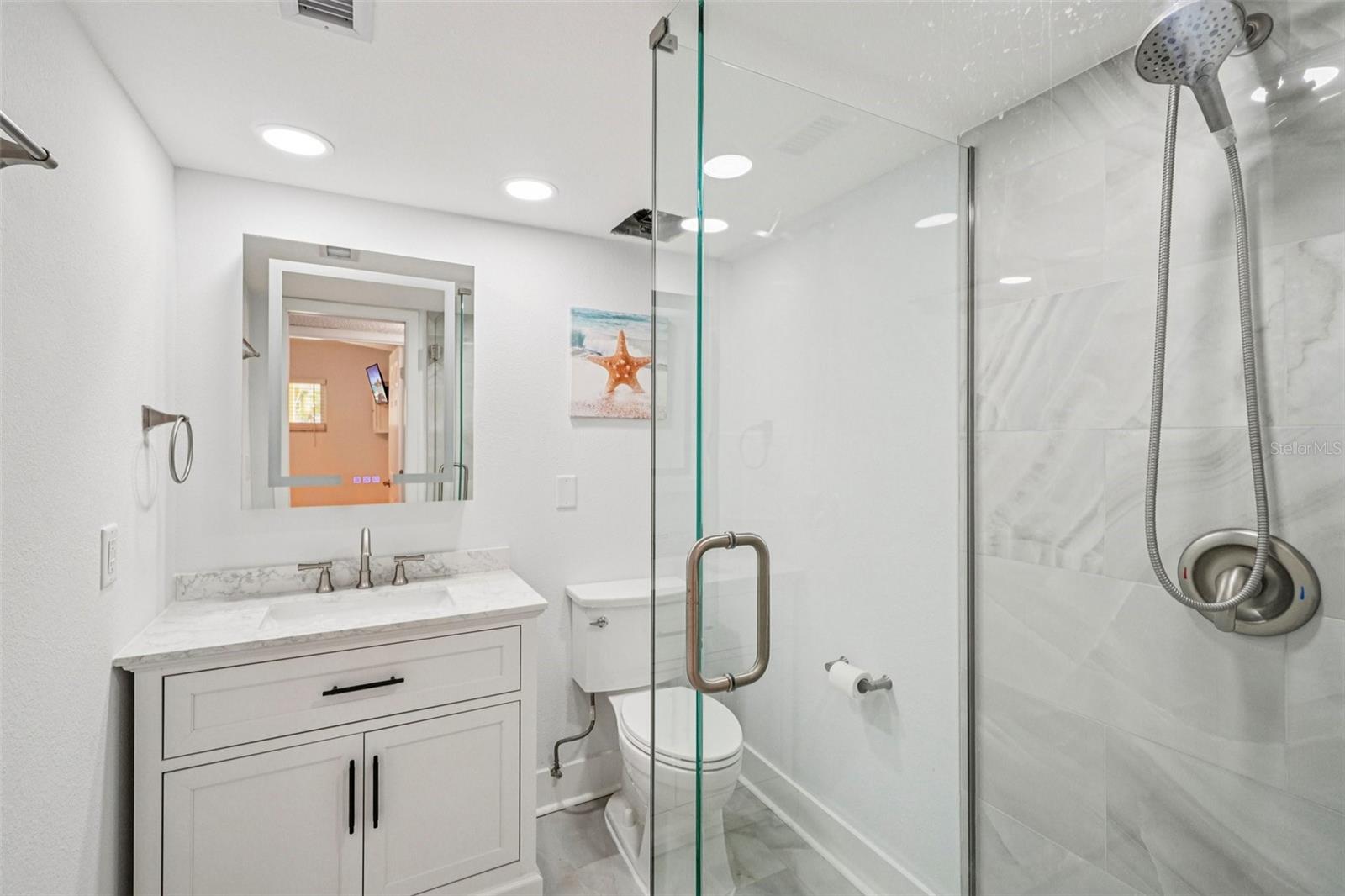Bathroom #2 (Fully Remodeled) This fully remodeled bathroom impresses with a frameless glass walk-in shower clad in marble-look tile, a white shaker-style vanity with quartz countertop, a backlit mirror, recessed lighting, and brushed nickel fixtures throughout a crisp, move-in-ready finish from top to bottom.