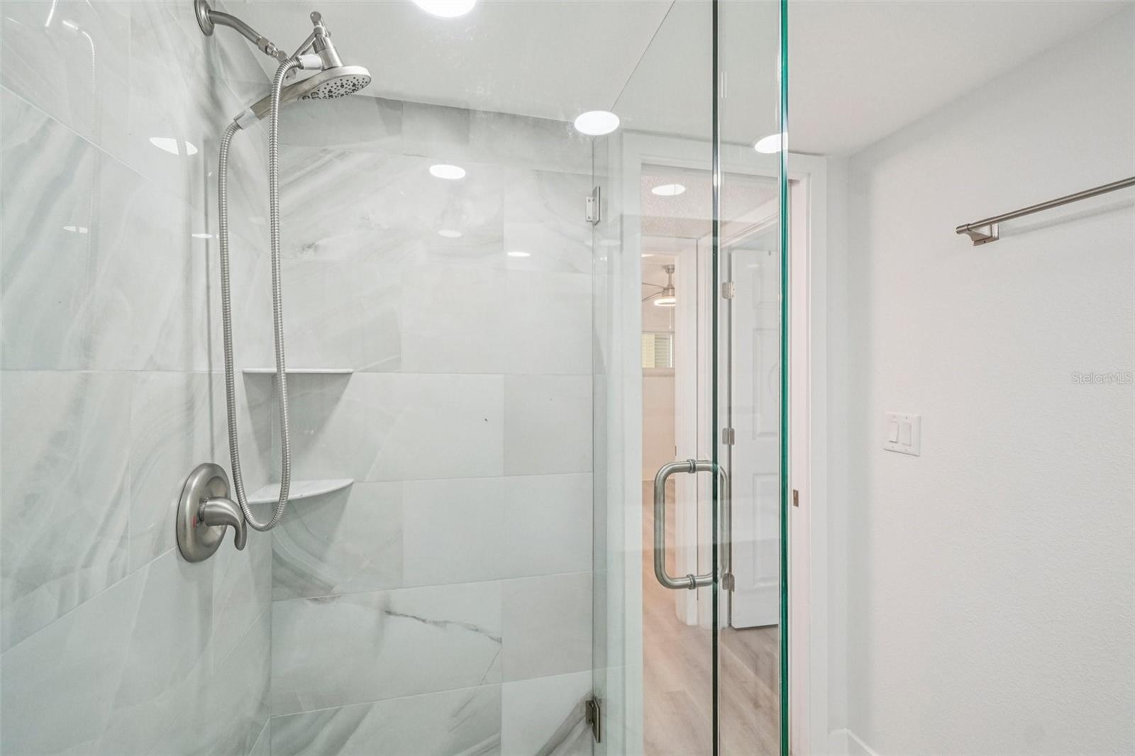 Bathroom #2 Shower Detail – This spa-inspired walk-in shower features floor-to-ceiling marble-look tile, a frameless glass enclosure, built-in corner shelving, and a handheld showerhead with brushed nickel fixtures a luxurious retreat designed with both style and function in mind.