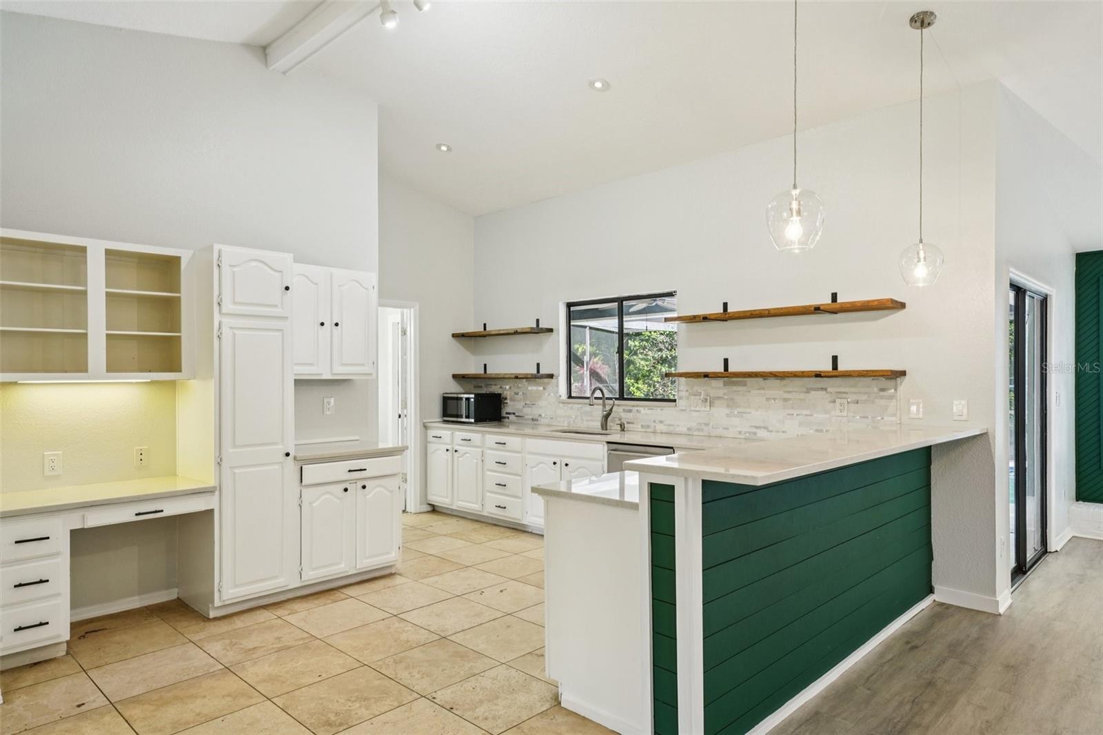 The spacious kitchen is well-equipped with quartz countertops, a tile backsplash, ample bright white cabinetry, stylish open wood shelving, a built-in desk, and stainless-steel appliances, including a new refrigerator. The breakfast bar, accented with charming shiplap detail, provides a comfortable spot for casual meals or morning coffee while naturally connecting to the family room.