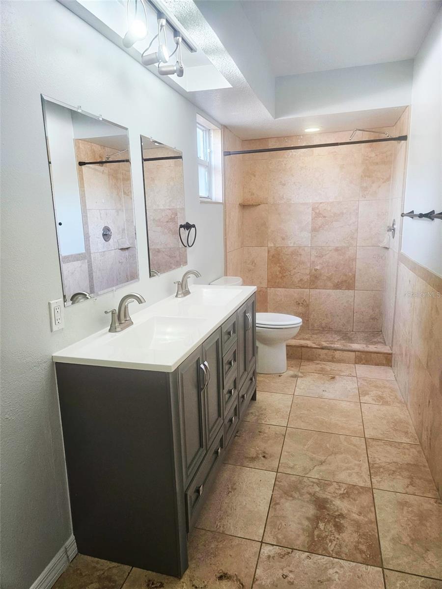 The primary suite boasts travertine flooring, an oversized walk-in closet, and an en-suite bathroom with a walk-in shower surrounded by beautiful travertine tile, and a brand-new dual-sink vanity.