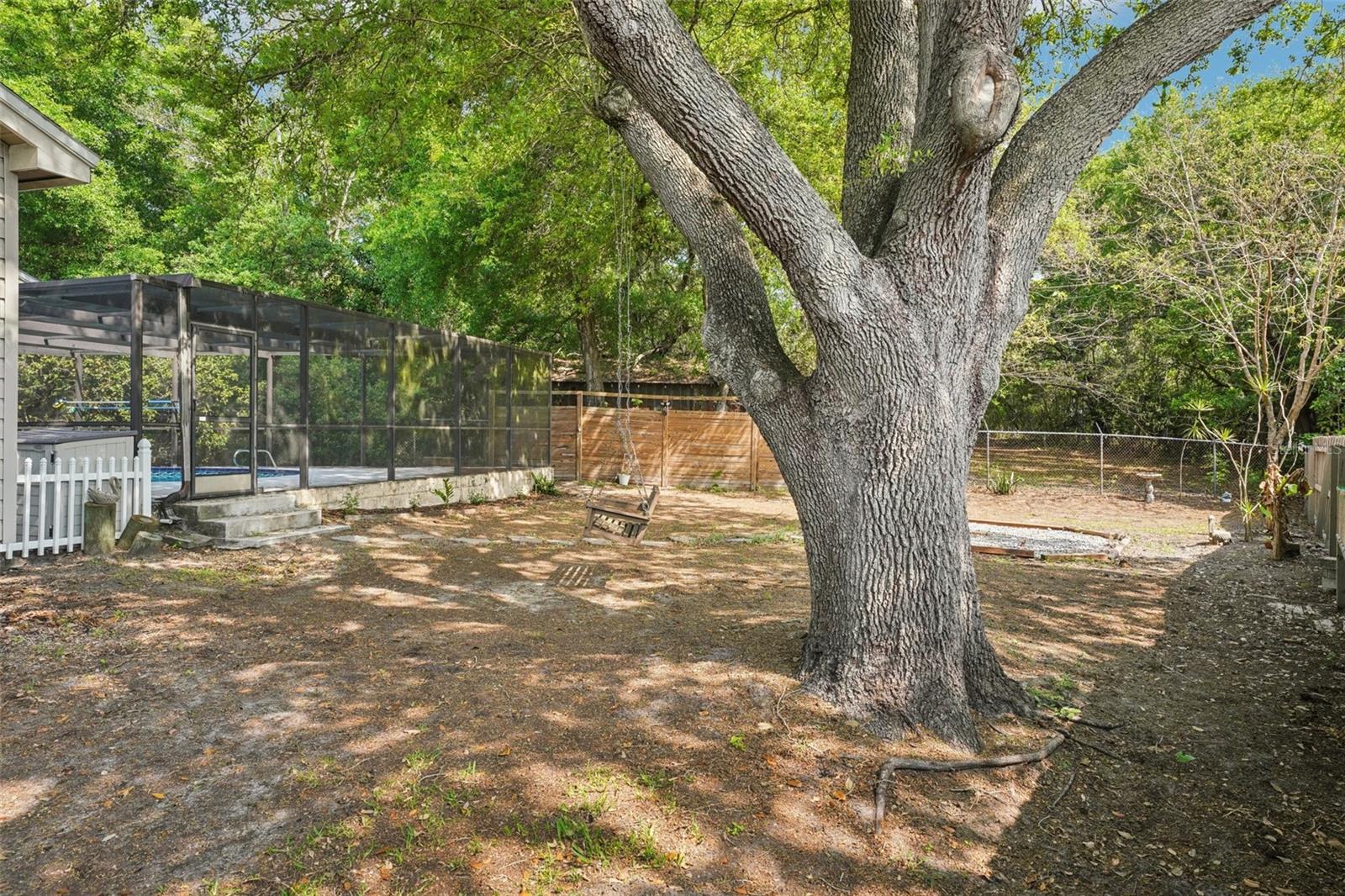 The expansive, fully fenced backyard features an enclosed outdoor shower area just off the pool with a rain shower head and handheld nozzle, while the side yards offer plenty of space to roam or garden, a playset, a swing under the mature oak, and a fire pit to gather around on cooler evenings.