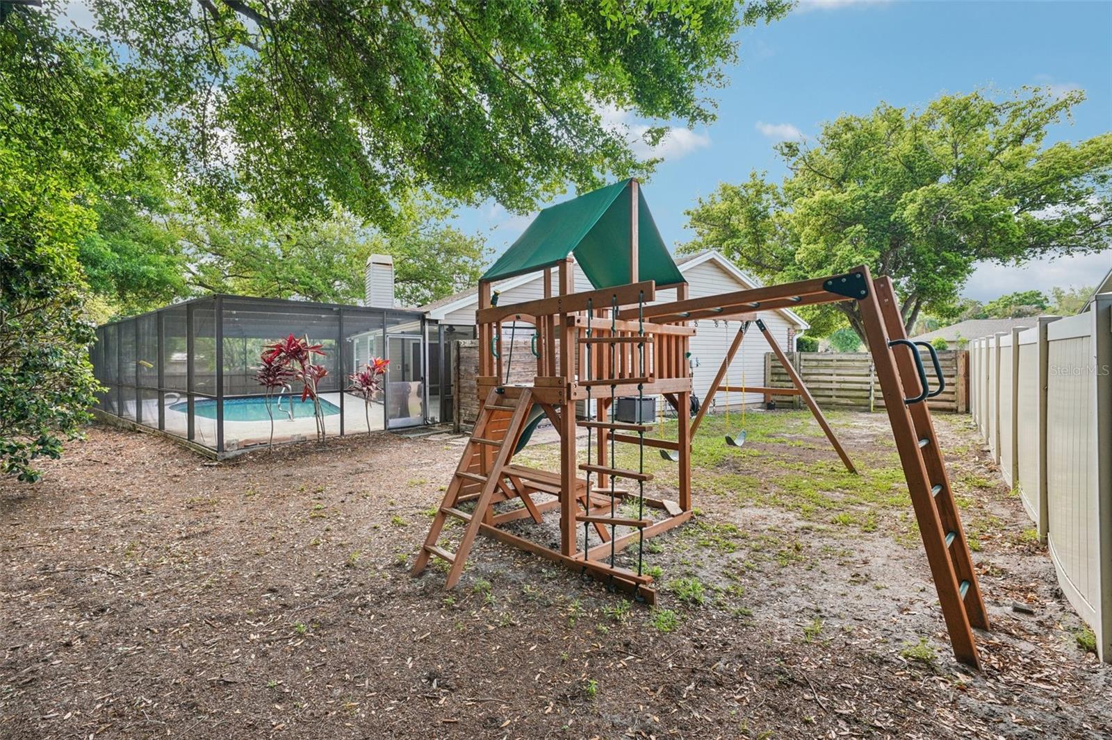 The expansive, fully fenced backyard features an enclosed outdoor shower area just off the pool with a rain shower head and handheld nozzle, while the side yards offer plenty of space to roam or garden, a playset, a swing under the mature oak, and a fire pit to gather around on cooler evenings.