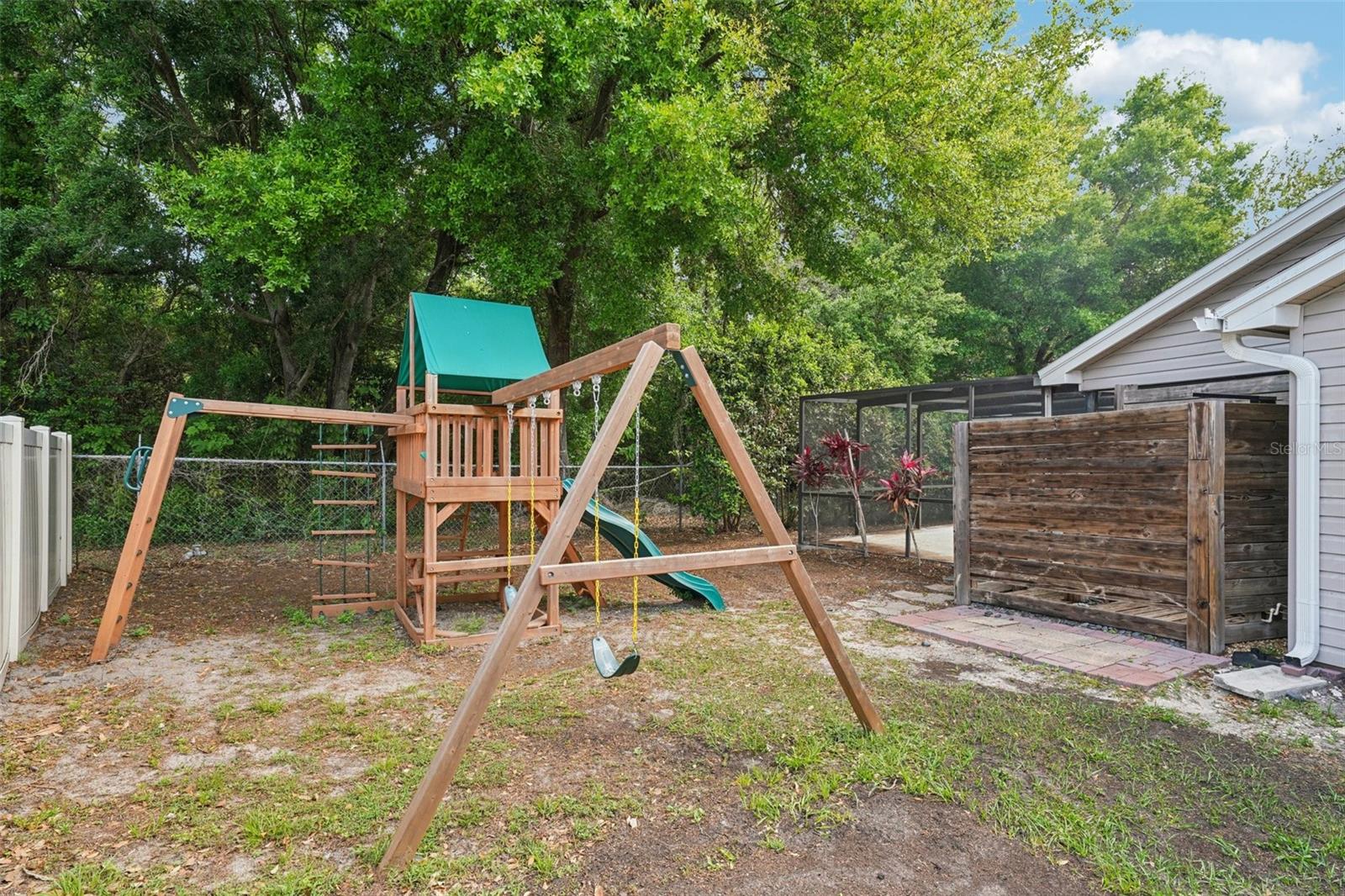 The expansive, fully fenced backyard features an enclosed outdoor shower area just off the pool with a rain shower head and handheld nozzle, while the side yards offer plenty of space to roam or garden, a playset, a swing under the mature oak, and a fire pit to gather around on cooler evenings.