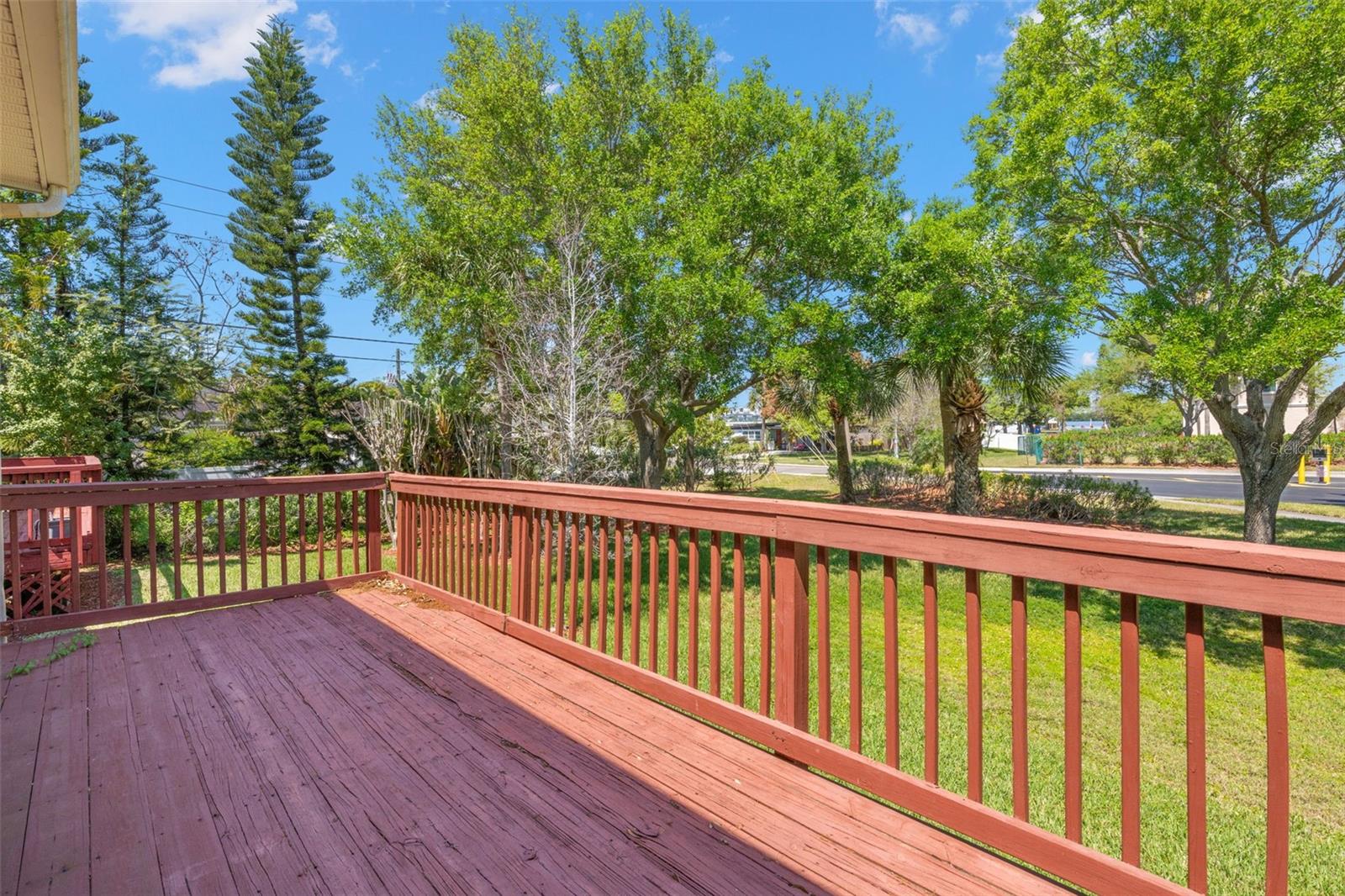 Elevated deck with open railing overlooks a green, tree-lined setting, providing a sense of space and a pleasant outdoor backdrop.