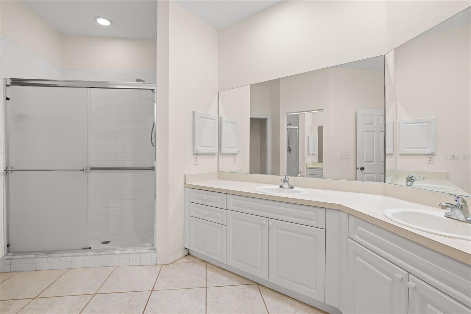 Spacious primary bathroom featuring an extended dual-sink vanity, abundant counter space, neutral tones, tile flooring and a full-width mirror that enhances light and openness.