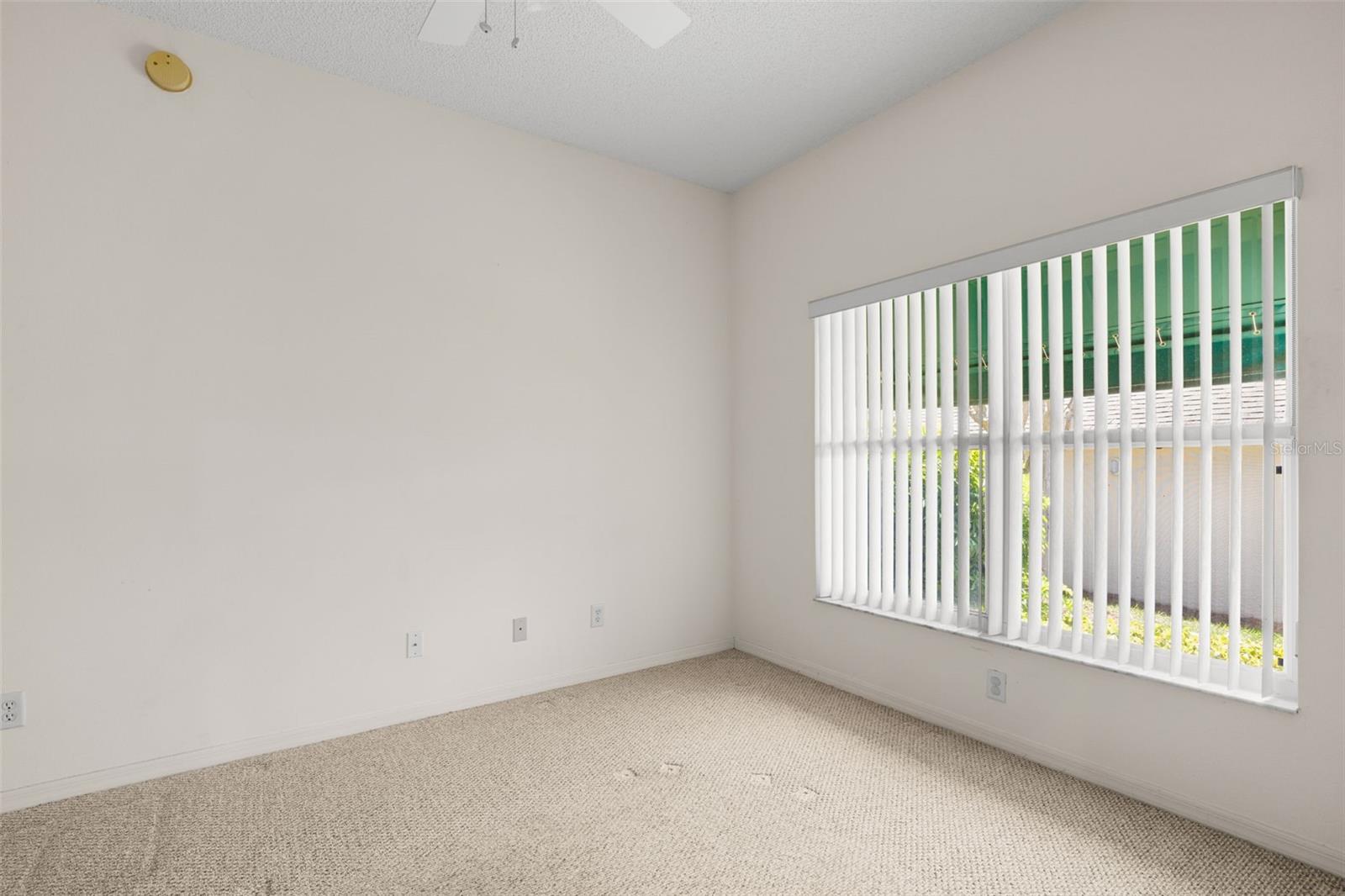 Versatile secondary bedroom with a large window for natural light, carpeted flooring, neutral tones, and a ceiling fan, offering flexibility as a guest room, home office, or additional living space.