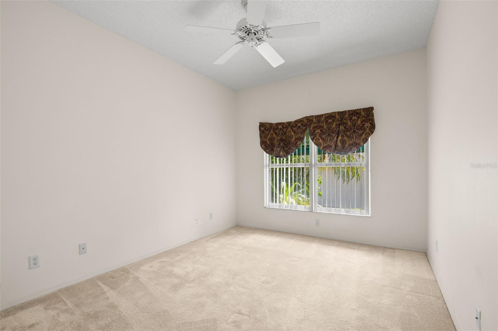 Bedroom 3 featuring a large window for natural light, carpeted flooring, neutral tones, and a ceiling fan, offering a comfortable and adaptable layout.