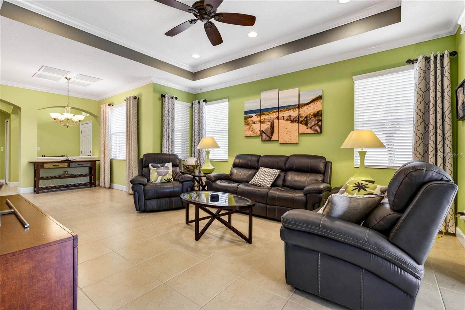 Living area with tray ceiling and crown molding as well as ceiling fan. Window treatments convey.