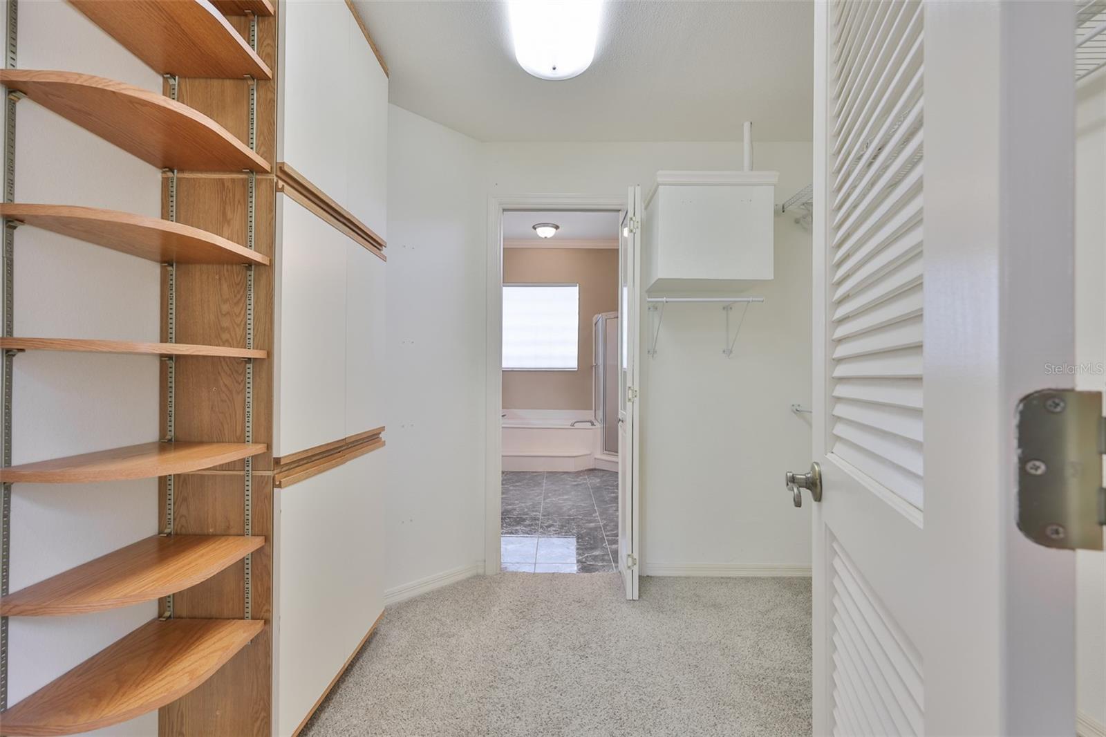 A large walk in closet with shelving and storage connects to the primary bedroom and bath.