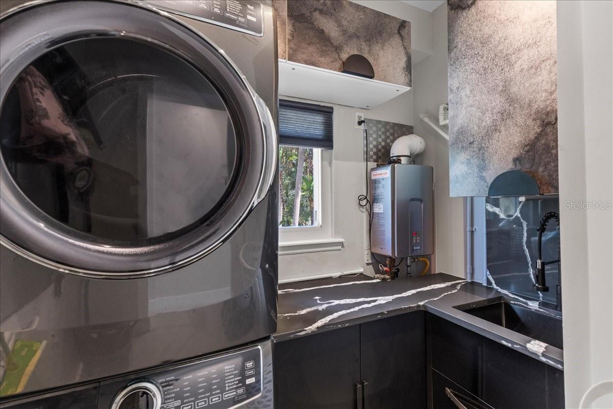 Dedicated laundry room with full size stacked washer/ dryer, tankless water heater, storage & utility sink