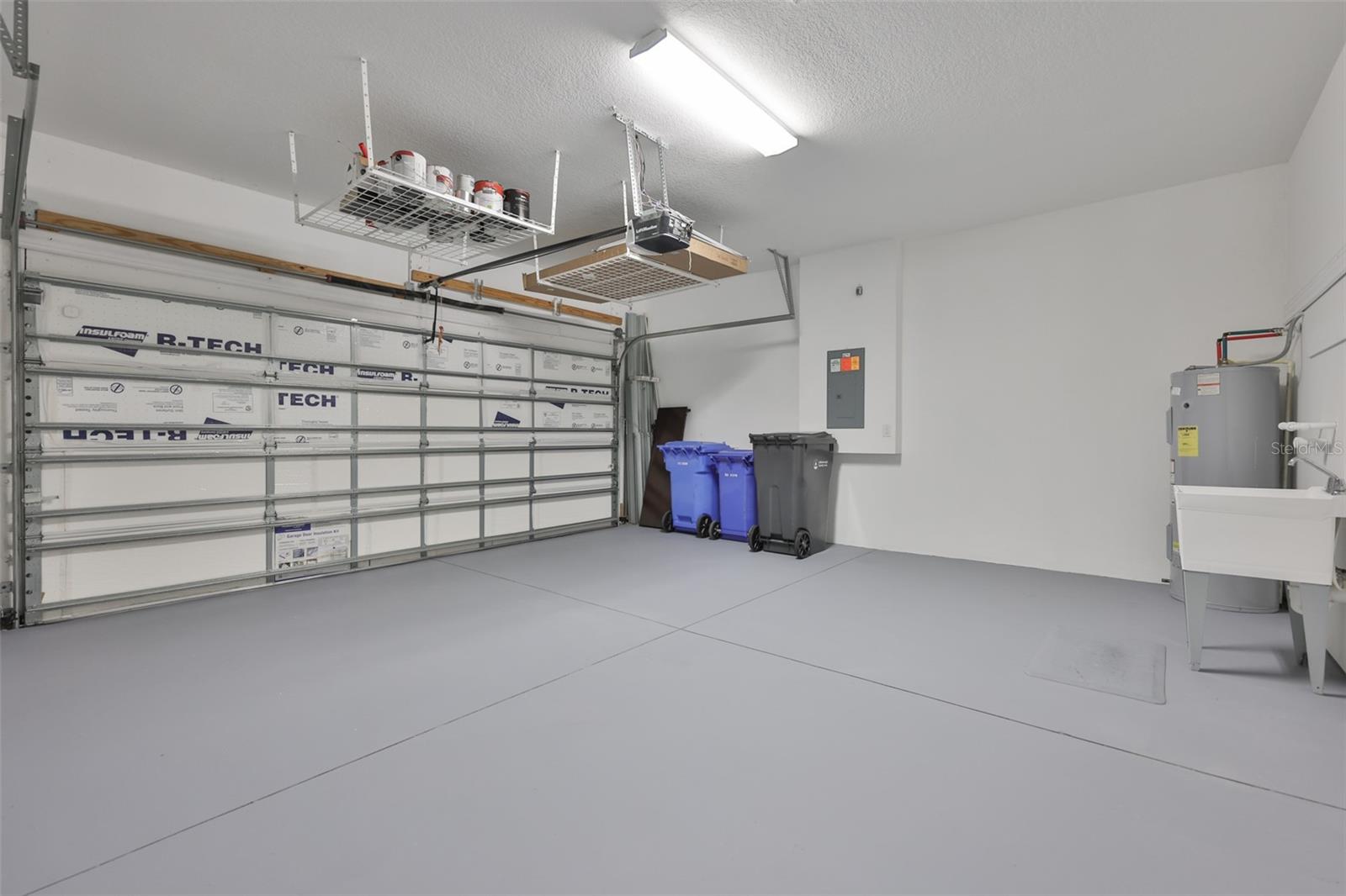 Garage offers overhead storage, utility sink and an insulated door.  Hurricane shutters are located to the very back of the picture.