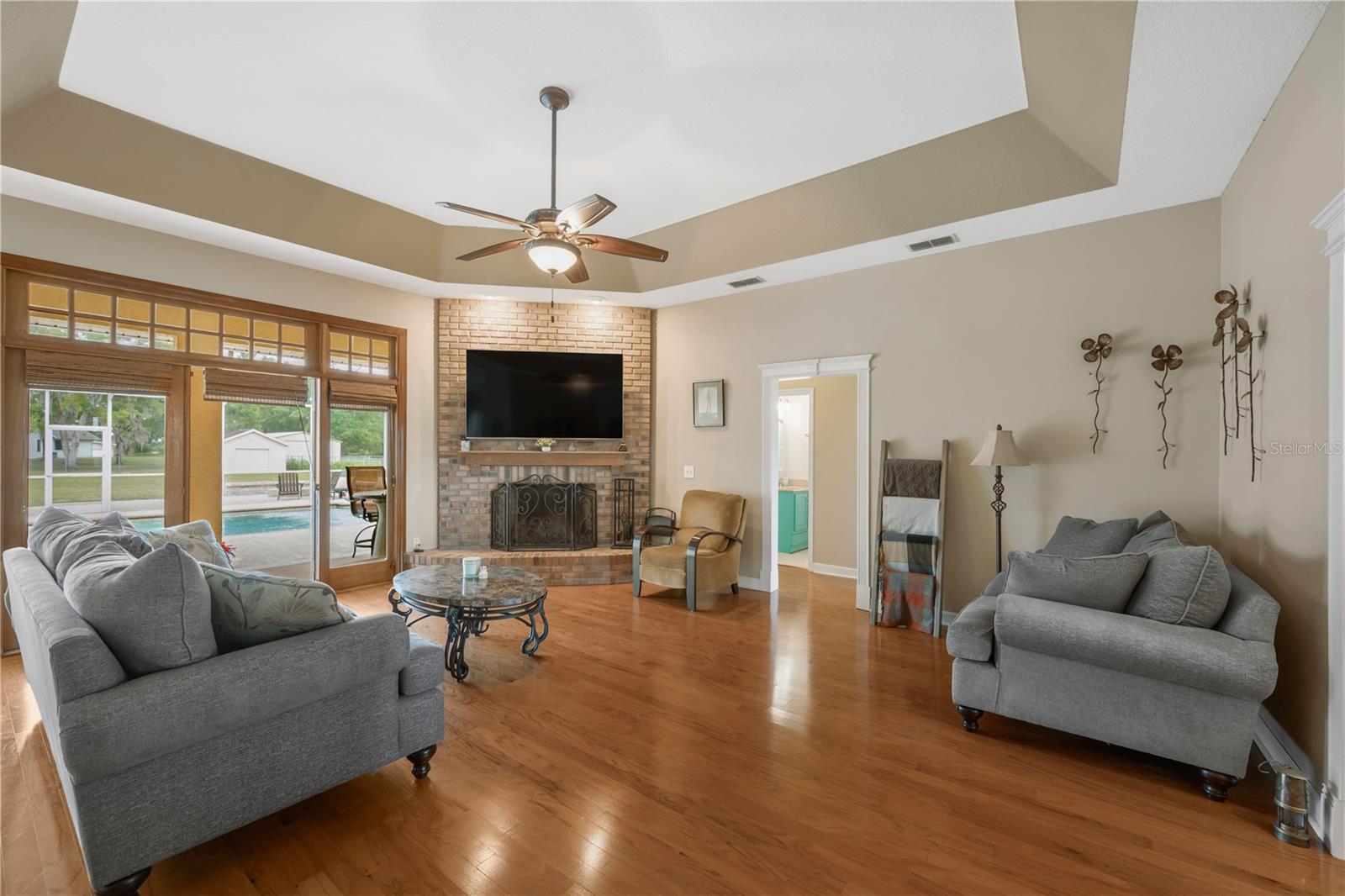 Spacious great room filled with natural light, soaring ceilings with tray, and a cozy wood-burning fireplace that is ideal for gathering with family or unwinding after a long day.
