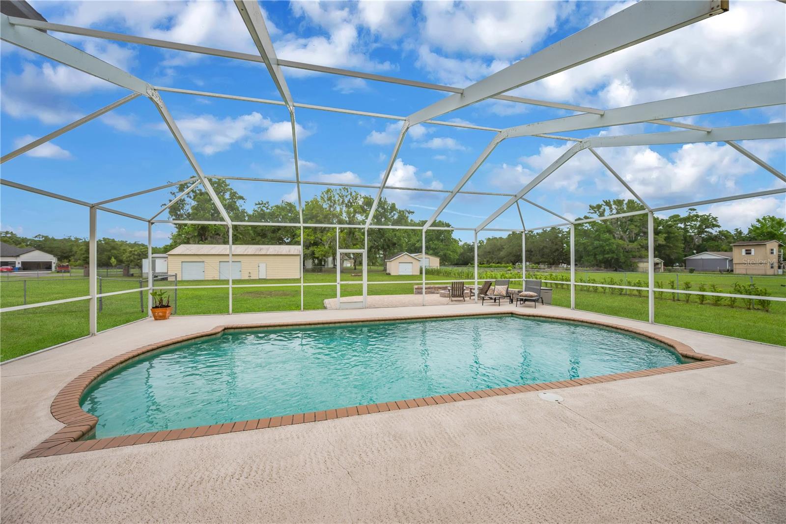 The backyard is designed for enjoying the Florida outdoors, featuring a screened pool, a recently installed paver patio with a firepit, a fully fenced yard perfect for pets to roam with a privacy hedge, an incredible 1,500 sq ft detached garage/workshop with two roll-up doors, a separate single-door entry and another 12x16 detached shed with a roll-up door for all your toys, hobbies, and gatherings.