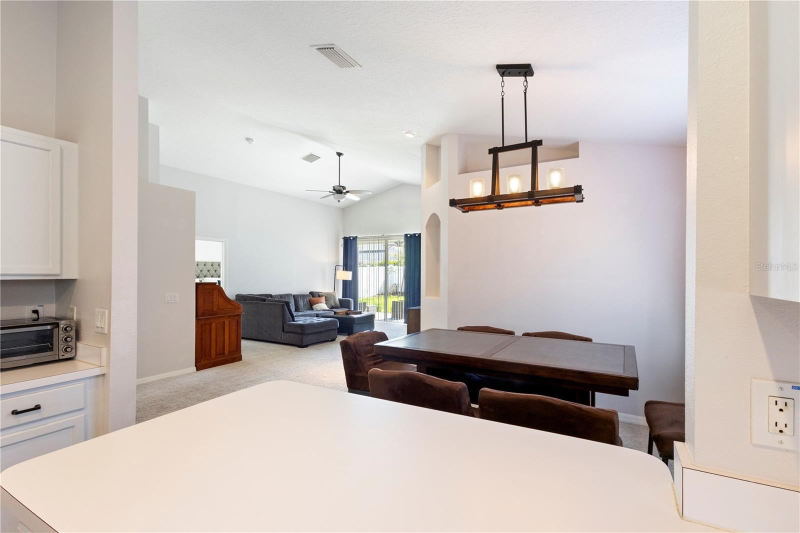 Spacious open-concept living and dining area featuring a modern chandelier, and seamless views into the inviting family room with sliding glass doors to the backyard.