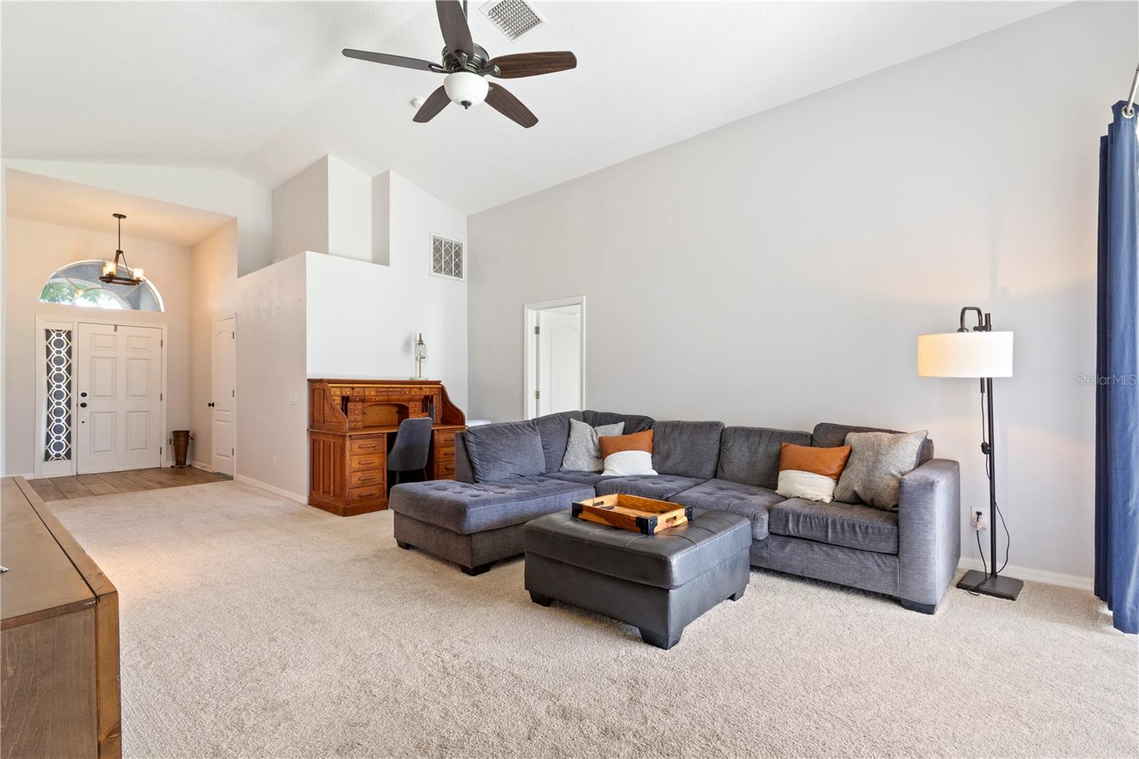 Spacious living room featuring high ceilings with a modern ceiling fan, built-in architectural details, and abundant natural light from the arched entryway.