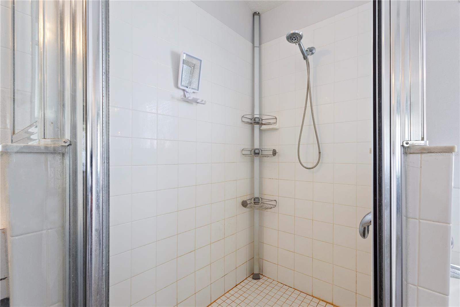 The walk-in shower features clean lined white tiles and corner storage for your shampoo and conditioner!
