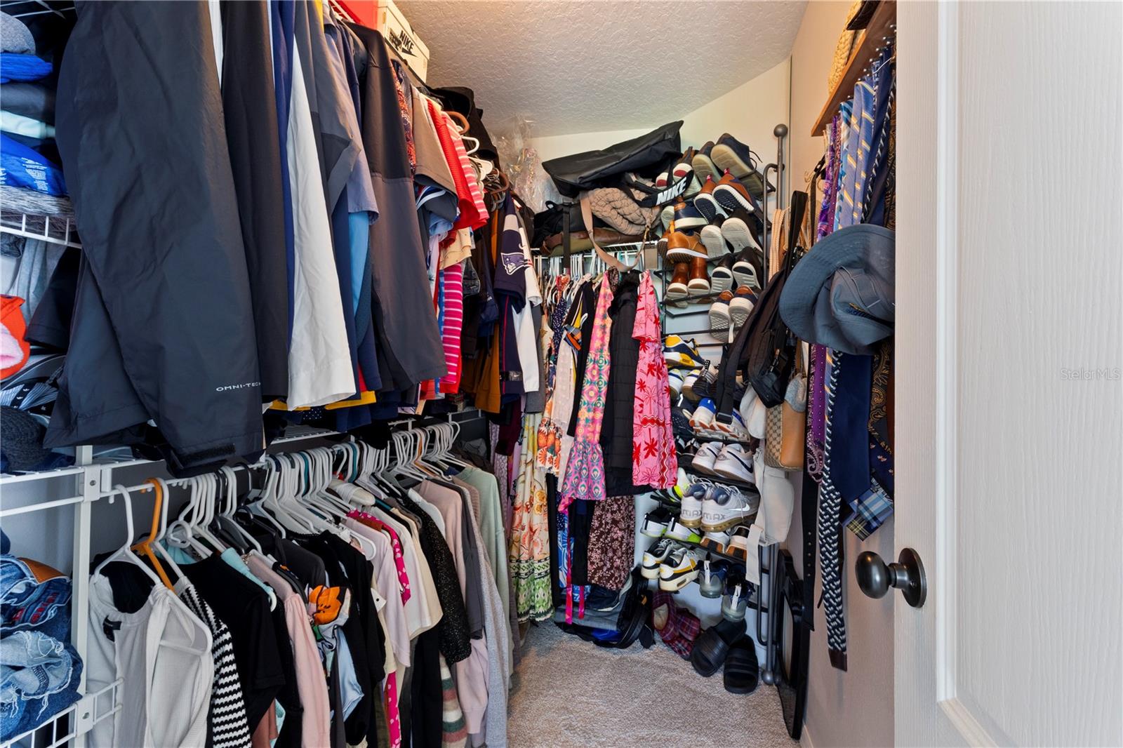 Spacious walk-in closet featuring extensive white wire shelving, double hanging rods packed with clothing, and abundant built-in storage for shoes, handbags, and accessories.