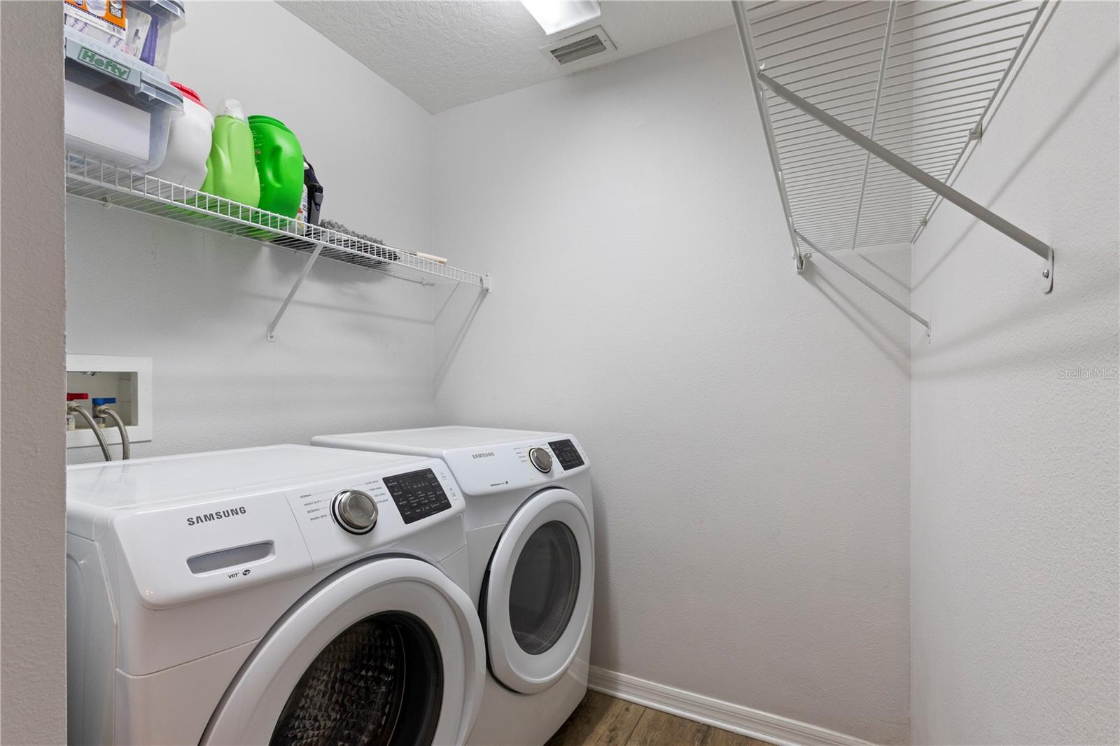 A tidy laundry room has shelving for storage and matching front load washer and dryer.