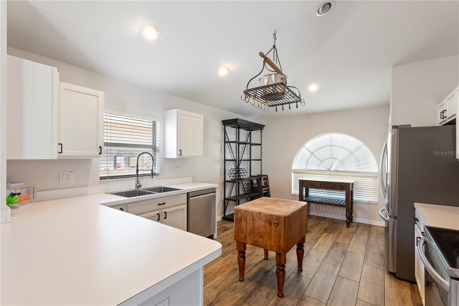 Stylish, light-filled kitchen boasting crisp white cabinetry, sleek countertops, stainless steel appliances, and a charming butcher block island on warm wood-look flooring.