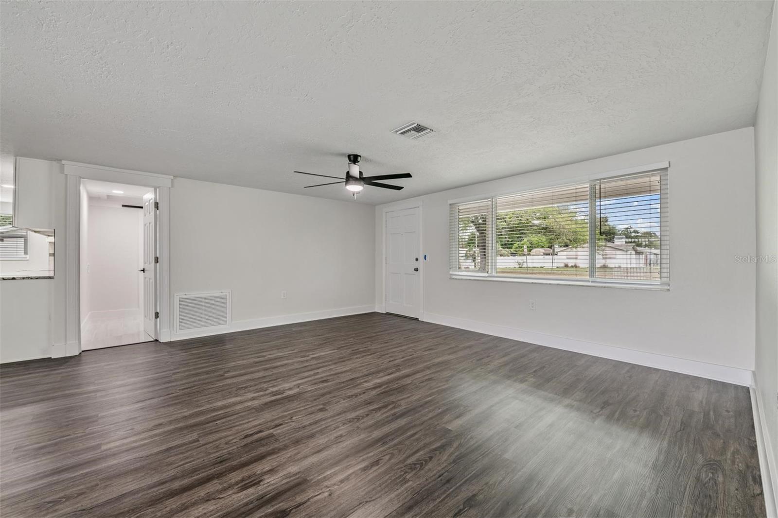 Living room area with door way into the laundry room, 2nd bath and garage area.  New flooring, HVAC ceiling vent, fan/light, windows and blinds