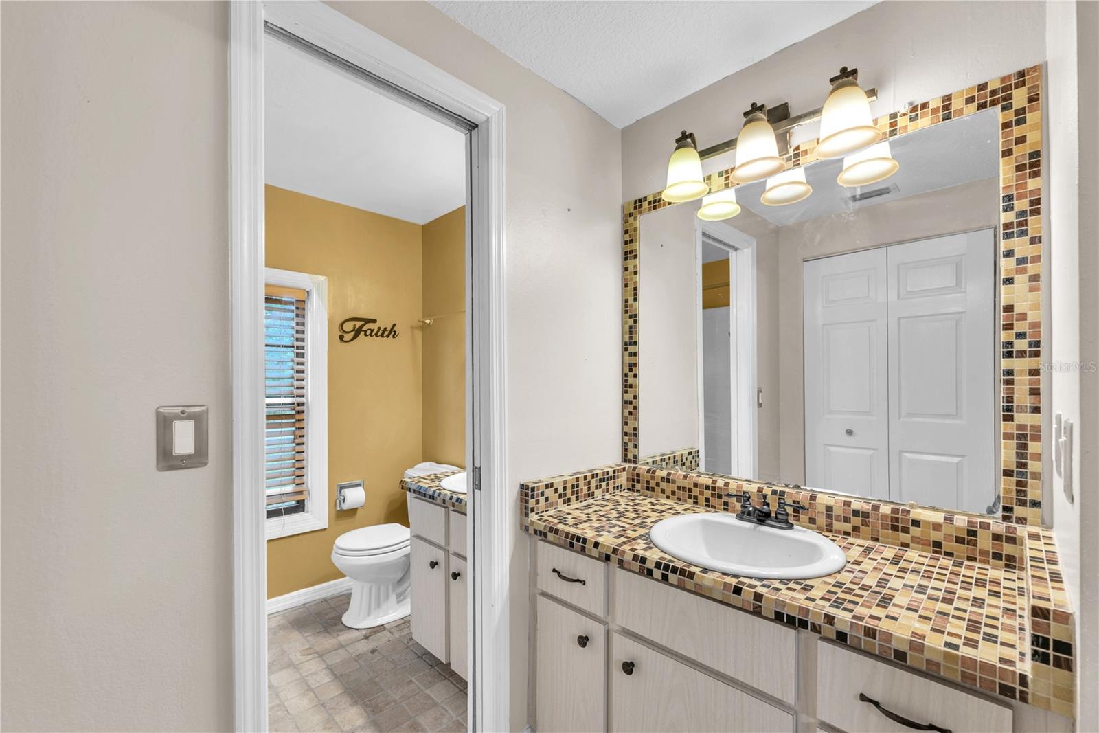 Second vanity and storage closet separated with a pocket door outside of full bathroom with tub/shower combination.