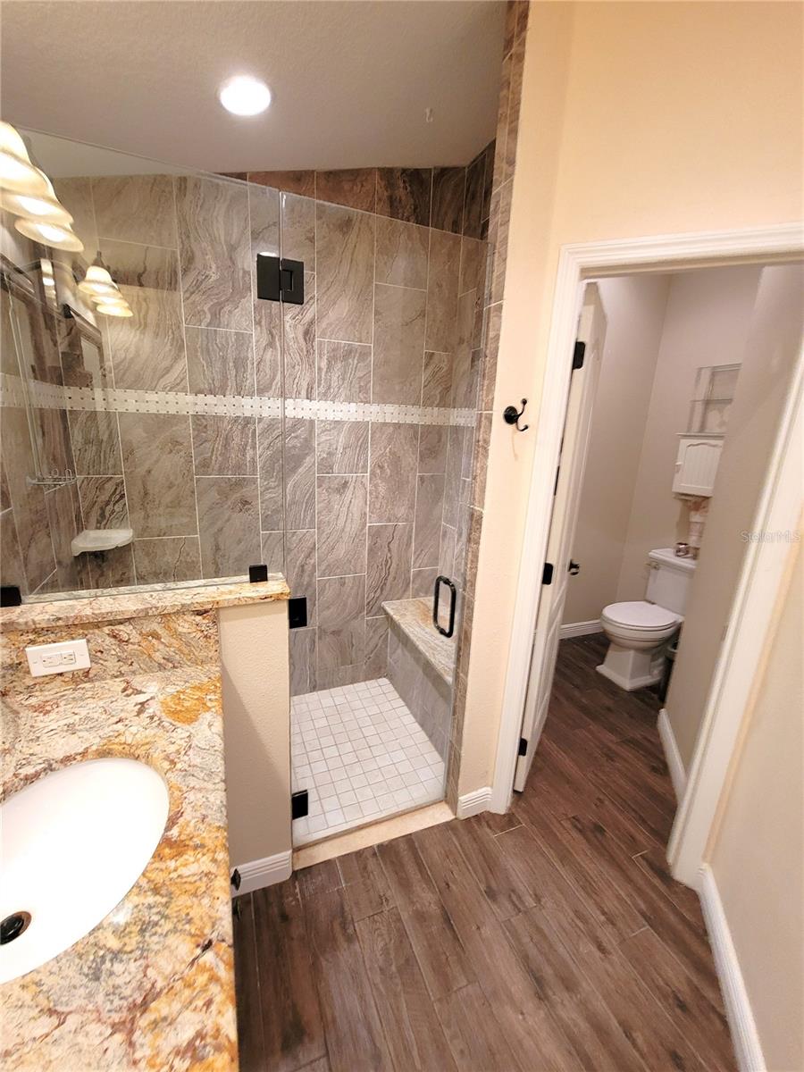 Private water closet and glass enclosed shower with granite bench