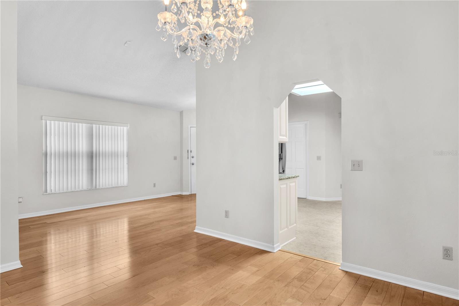 Formal Dining and Living rooms enhanced by light-toned engineered wood flooring and a beautiful chandelier that adds elegance to the dining space.