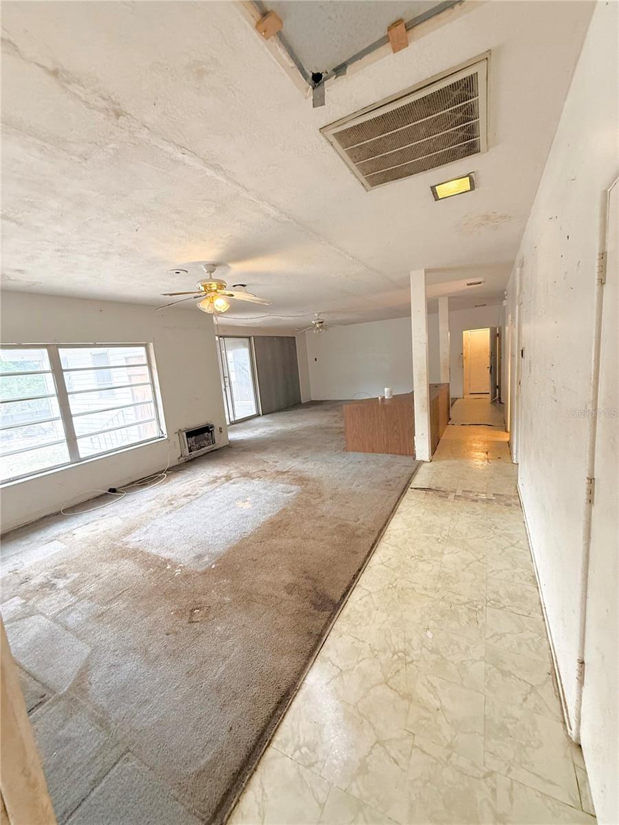 Spacious open-concept living and dining area featuring large windows for natural light, built-in shelving/bar area, and sliding glass door access to the enclosed patio. Excellent opportunity to redesign and modernize the expansive layout.