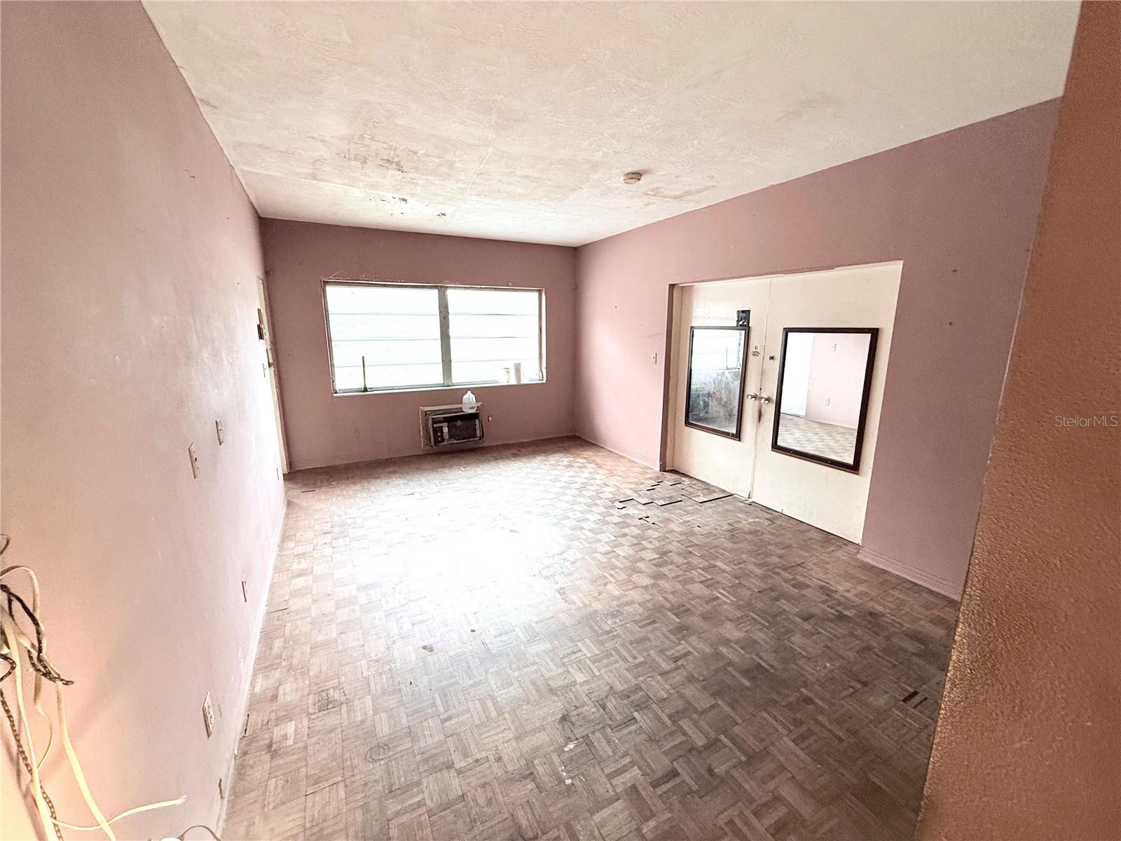 Generously sized bedroom with parquet wood flooring, large window for natural light, and adjoining bath access. Great footprint for a modern bedroom transformation.
