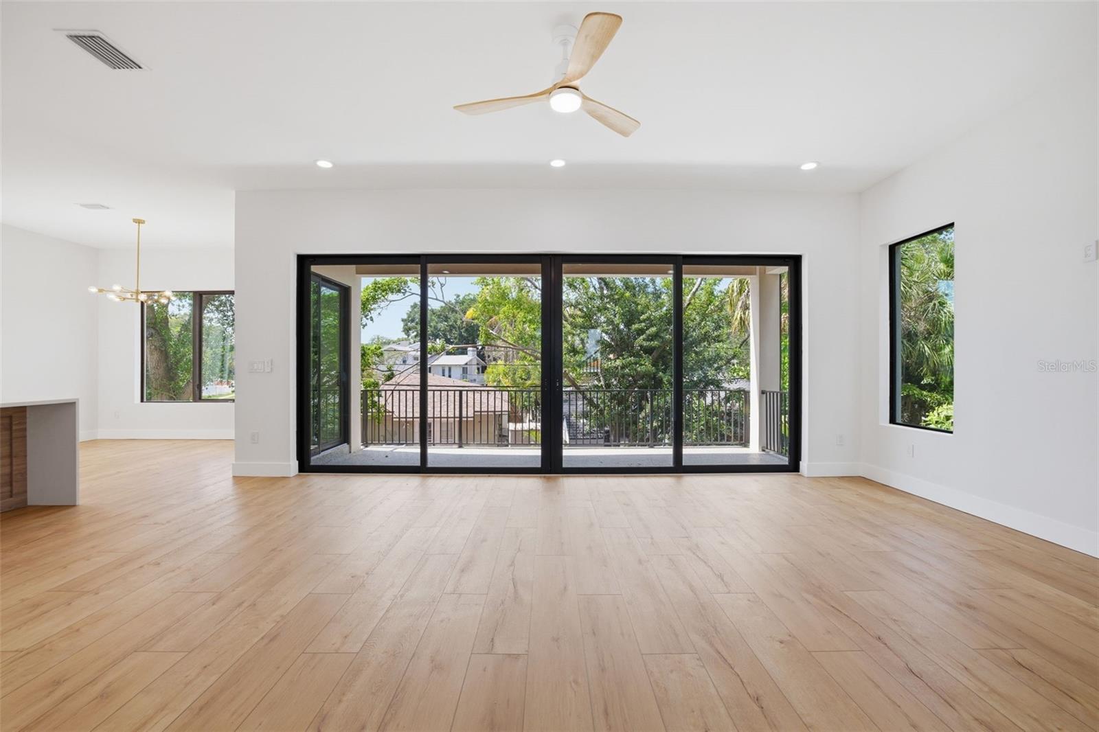 Main living area with a wall of sliders opening to balcony, overlooking back yard
