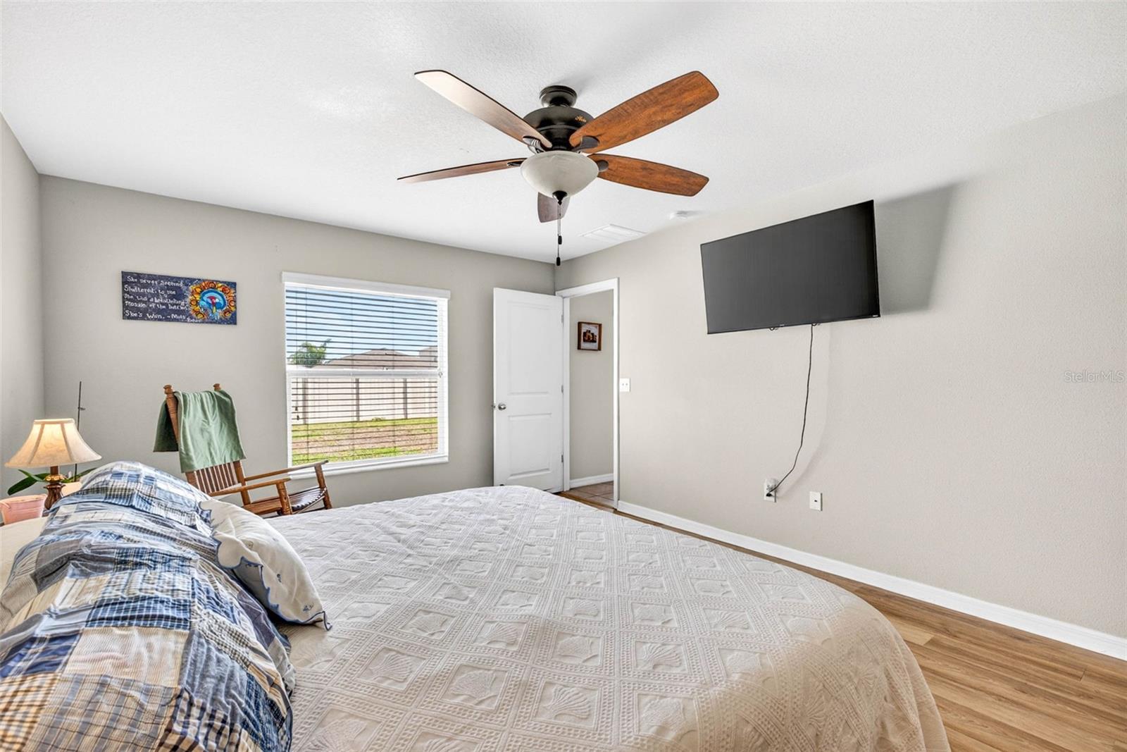 Primary bedroom with large picture window, ceiling fan, luxury vinyl plank flooring.