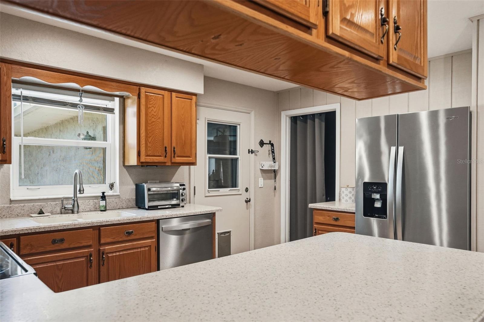 Large U-Shaped Kitchen with Natural Light Window over the Sink, Open to Living Room, Bar Stool Seating Area, Solid Surface Counters and Integral Sink for easy maintenance, and Double Door Pantry Closet