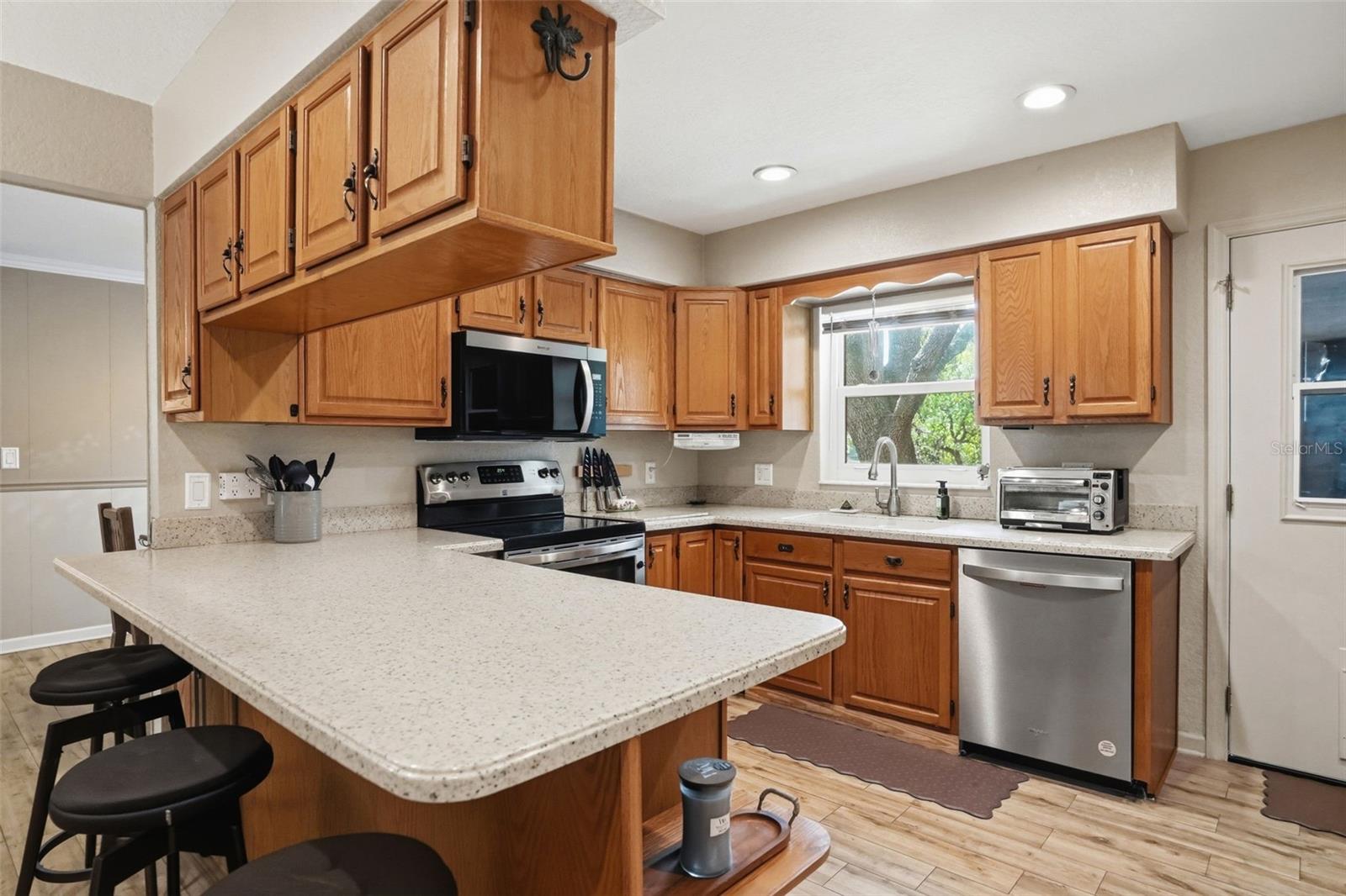 Large U-Shaped Kitchen with Natural Light Window over the Sink, Open to Living Room, Bar Stool Seating Area, Solid Surface Counters and Integral Sink for easy maintenance, and Double Door Pantry Closet