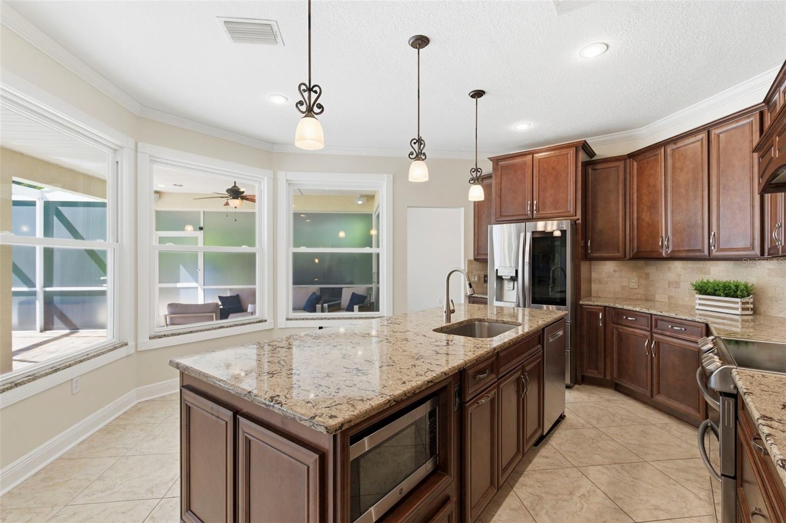 Beautifully appointed kitchen designed for both everyday living and entertaining, featuring rich wood cabinetry, granite countertops, and a large center island with seating. Stainless steel appliances, decorative range hood, and custom tile backsplash add a refined touch, while pendant lighting and recessed lighting create a warm, inviting atmosphere. The oversized island serves as the perfect gathering space for casual dining, hosting, or staying connected with family and guests.